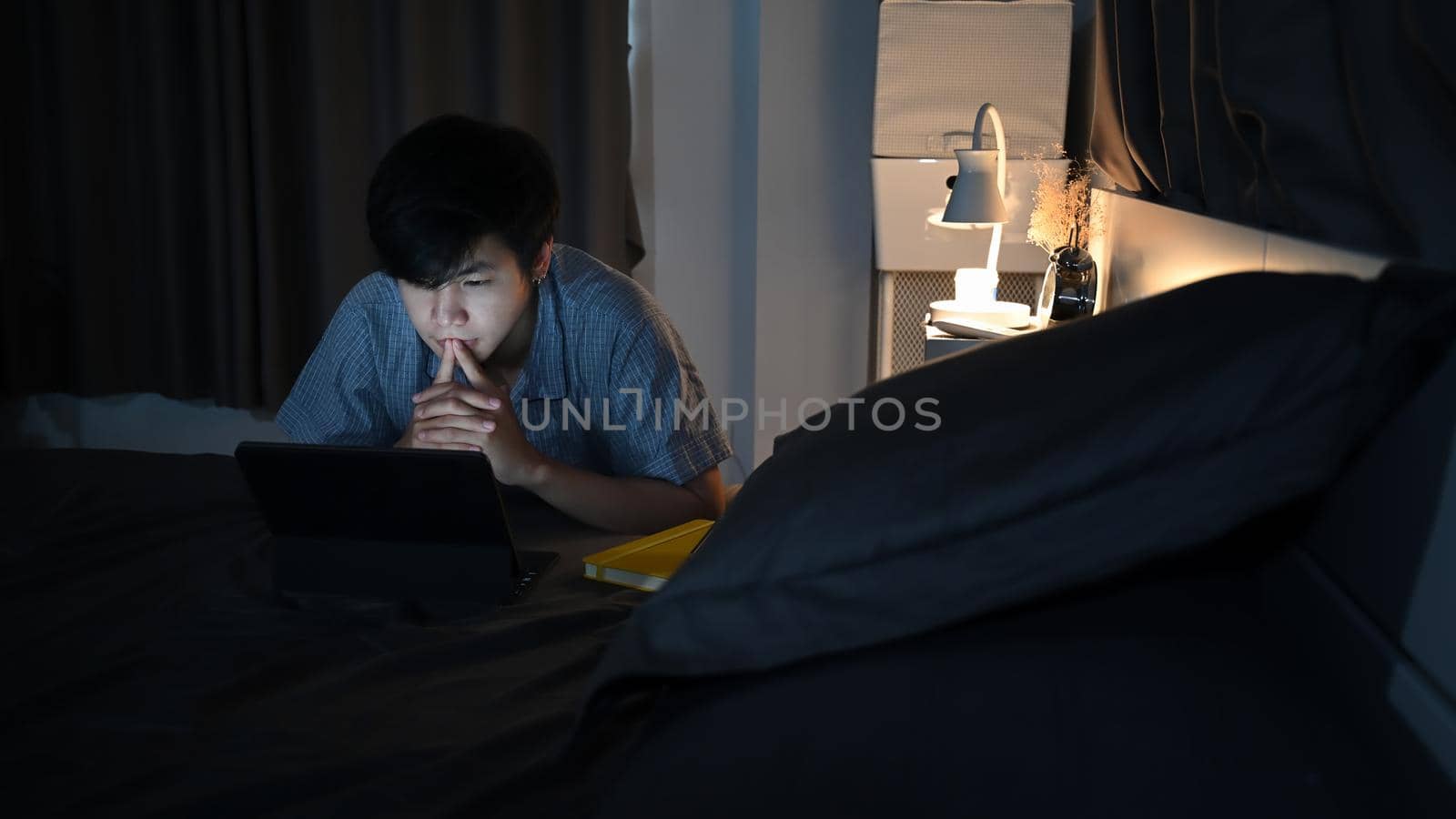 Young asian man lying on his bed and surfing inter.net with computer laptop.