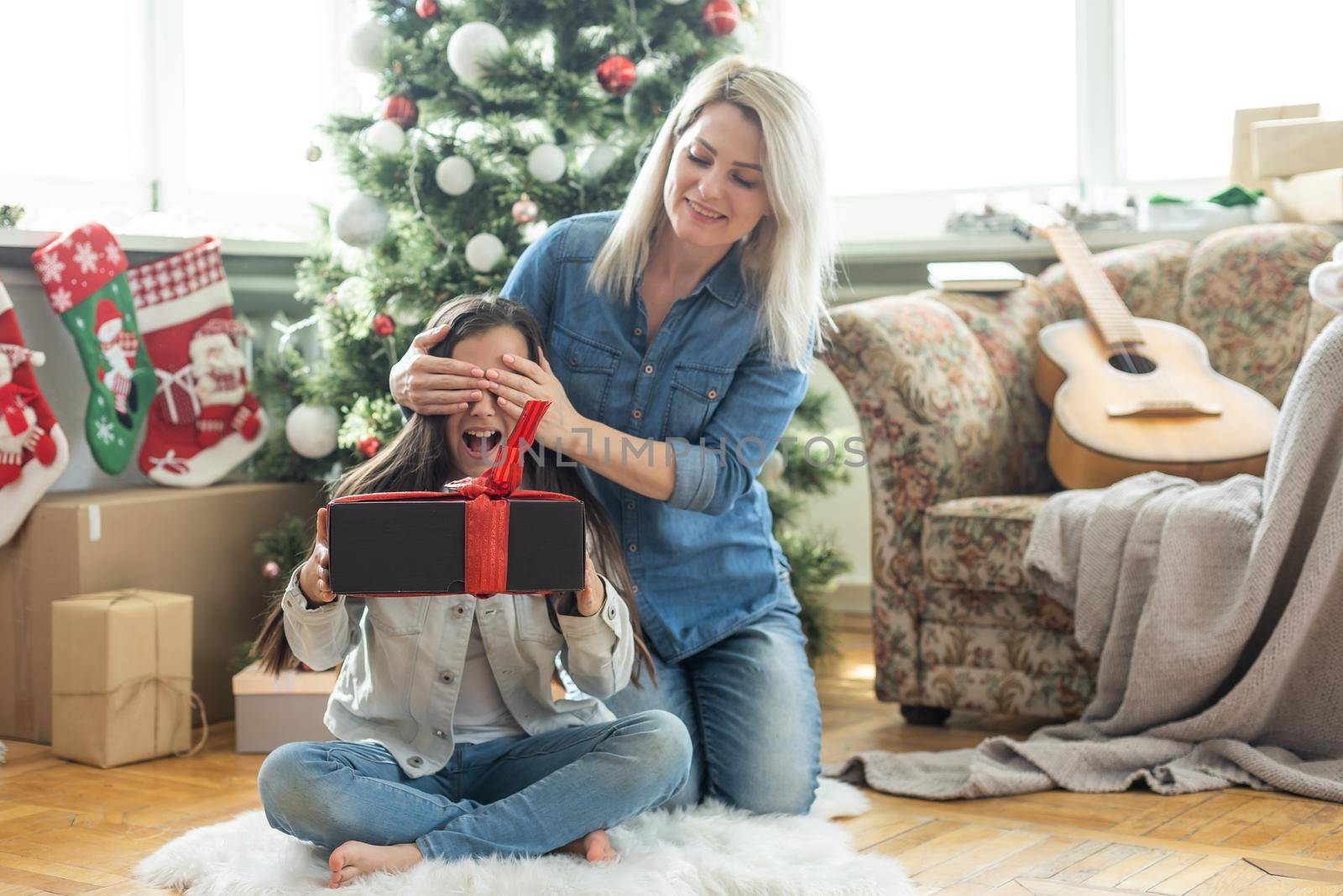 Merry Christmas and Happy Holidays. Cheerful mother and her cute daughter girl exchanging gifts. Mom and little child having fun near tree indoors. Loving family with presents in room by Andelov13