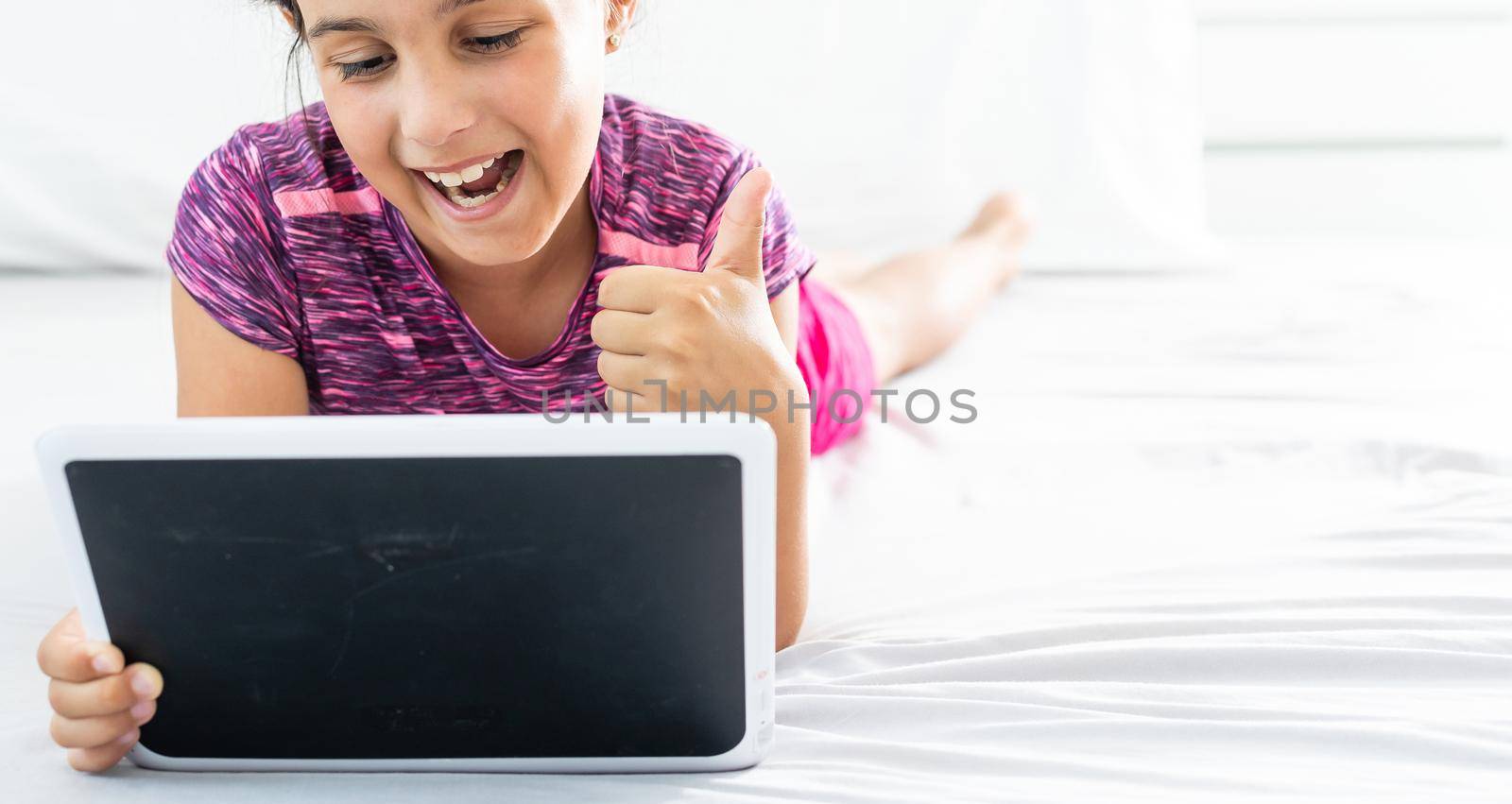 home, leisure, new technology and music concept - smiling little girl with tablet pc computer and headphones at home by Andelov13