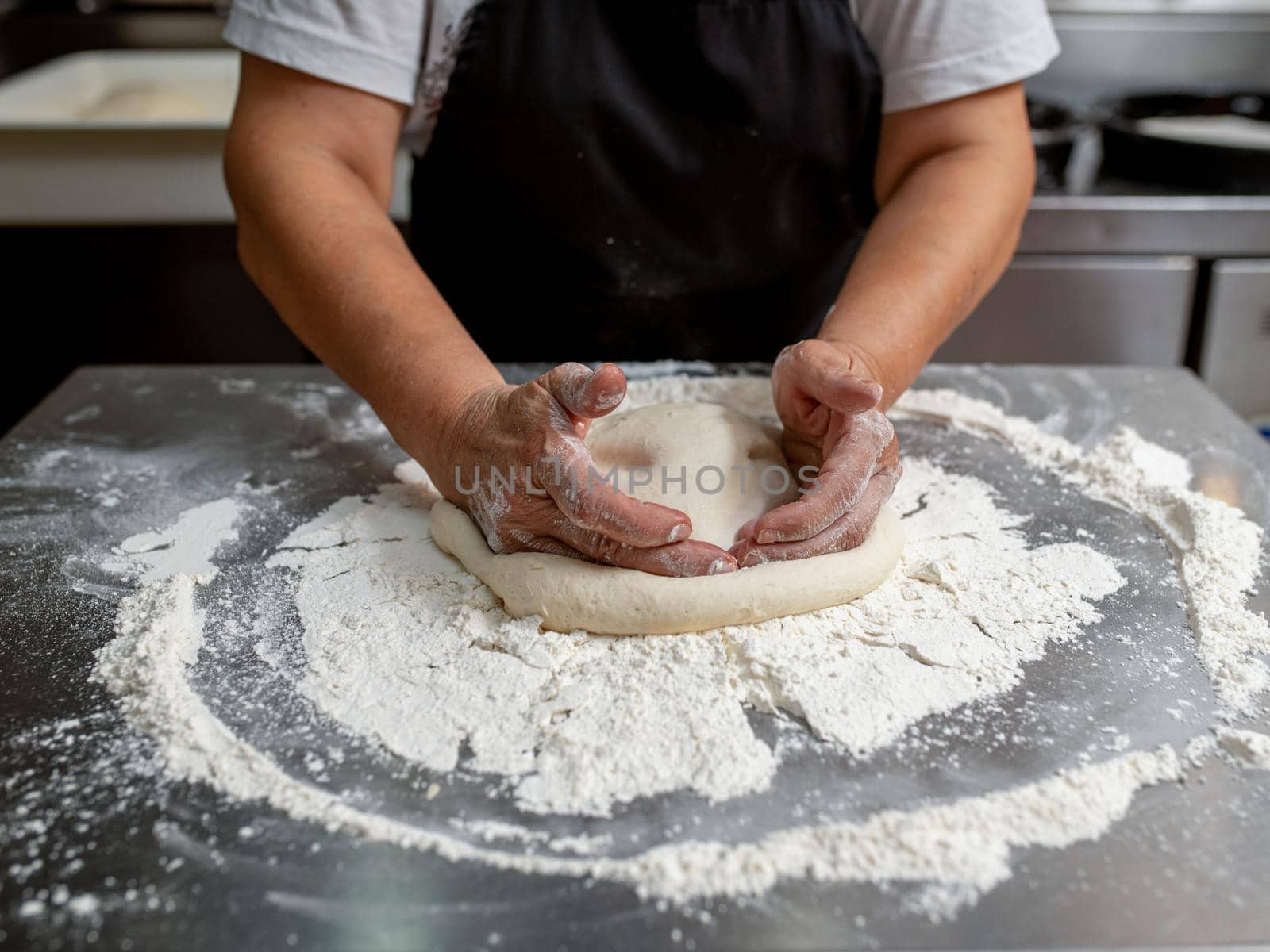 Woman making pizza dough on stainless steel counter by Sonat