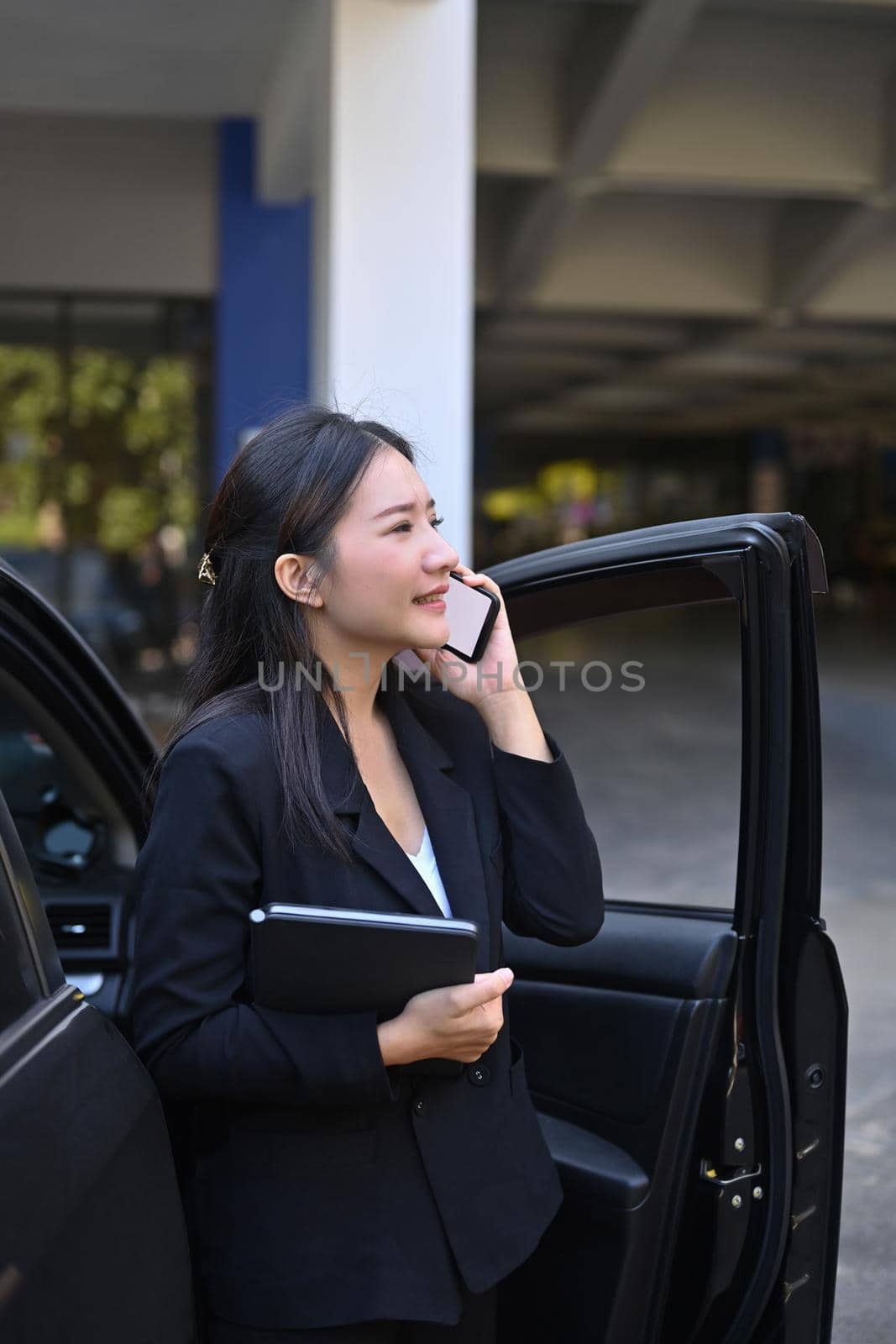 Confident businesswoman standing near her car and talking on mobile phone. by prathanchorruangsak