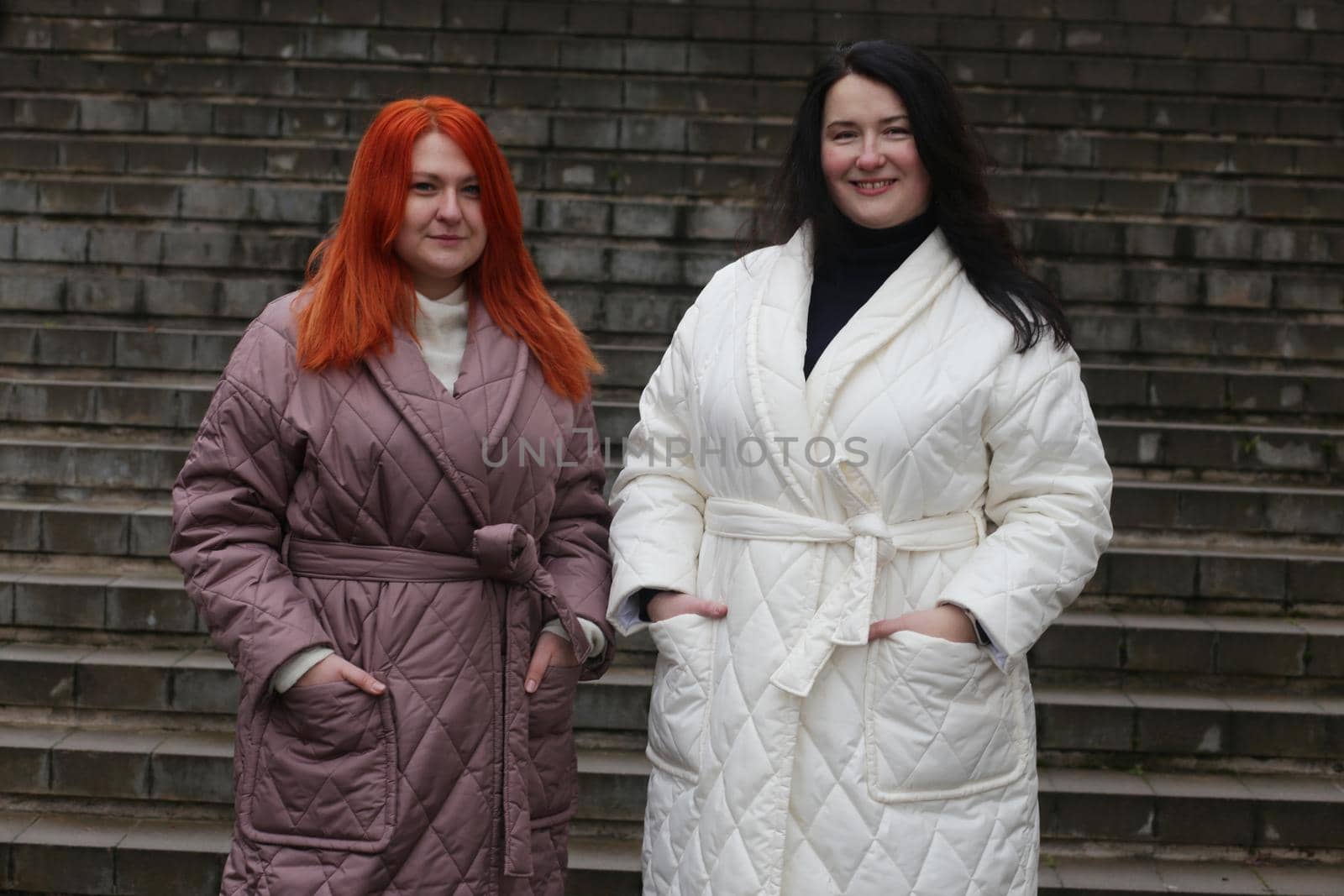 Two plus-size women posing in coats against a staircase backdrop. by gelog67