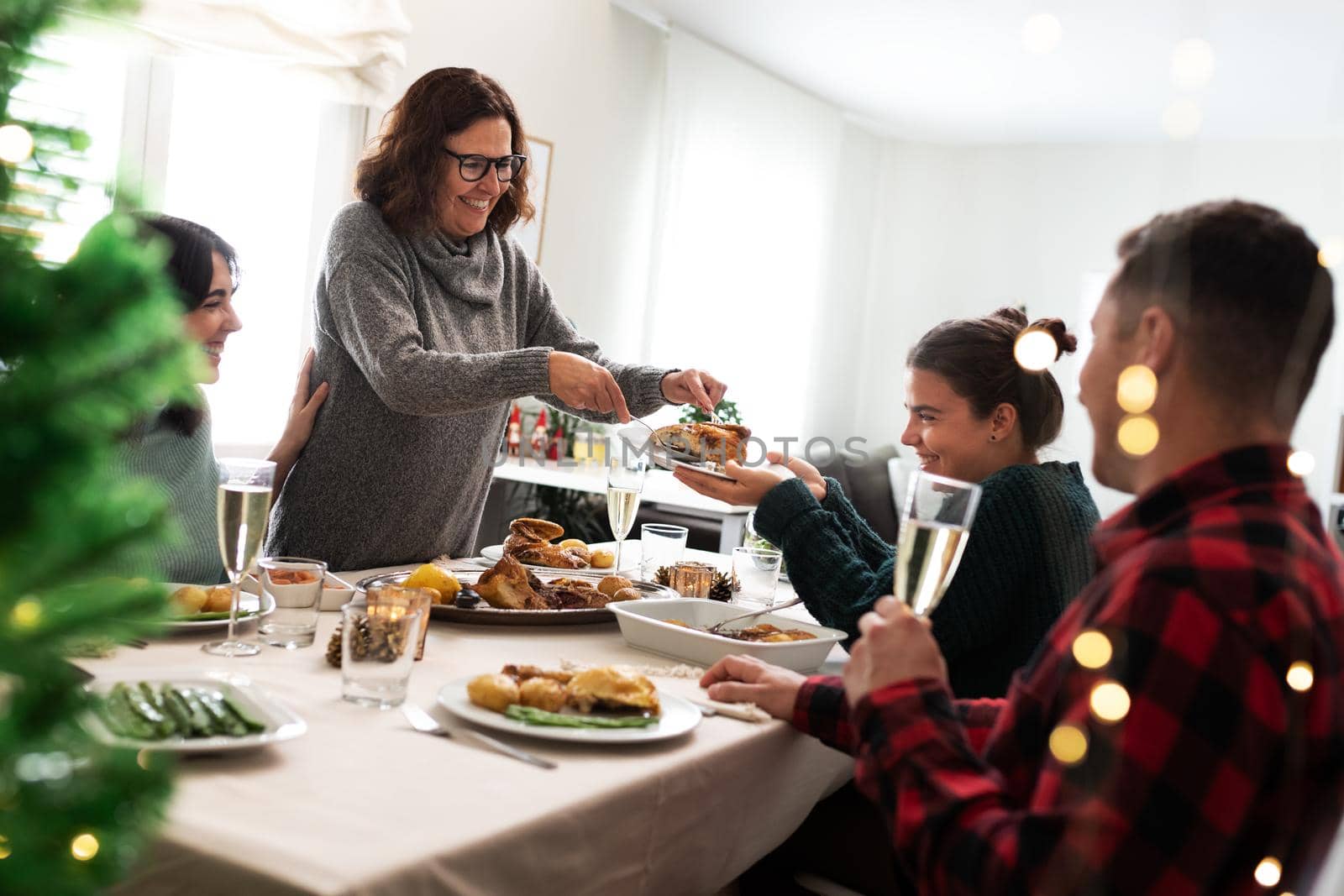 Happiness for Christmas. Smiling caucasian family have Christmas meal together. Mother serves daughter roasted chicken. by Hoverstock
