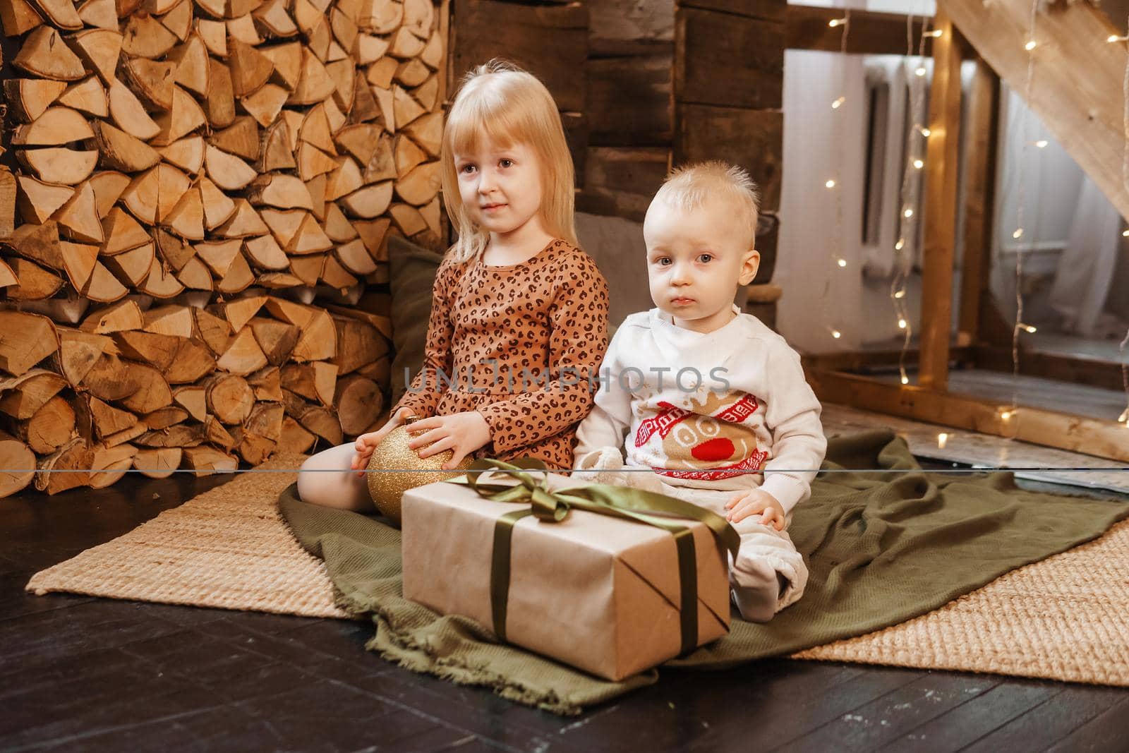 Little brother and sister play on Christmas eve in a beautiful house decorated for the New Year holidays. Children are playing with a Christmas gift. Scandinavian-style interior with live fir trees and a wooden staircase.