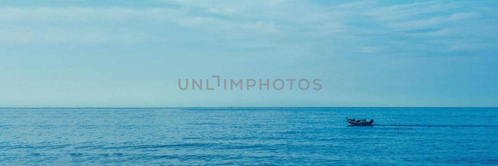 Simple background Calm dark blue sea fishing boat alone white pale Spindrift clouds Open way no limitations. BANNER LONG FORMAT.