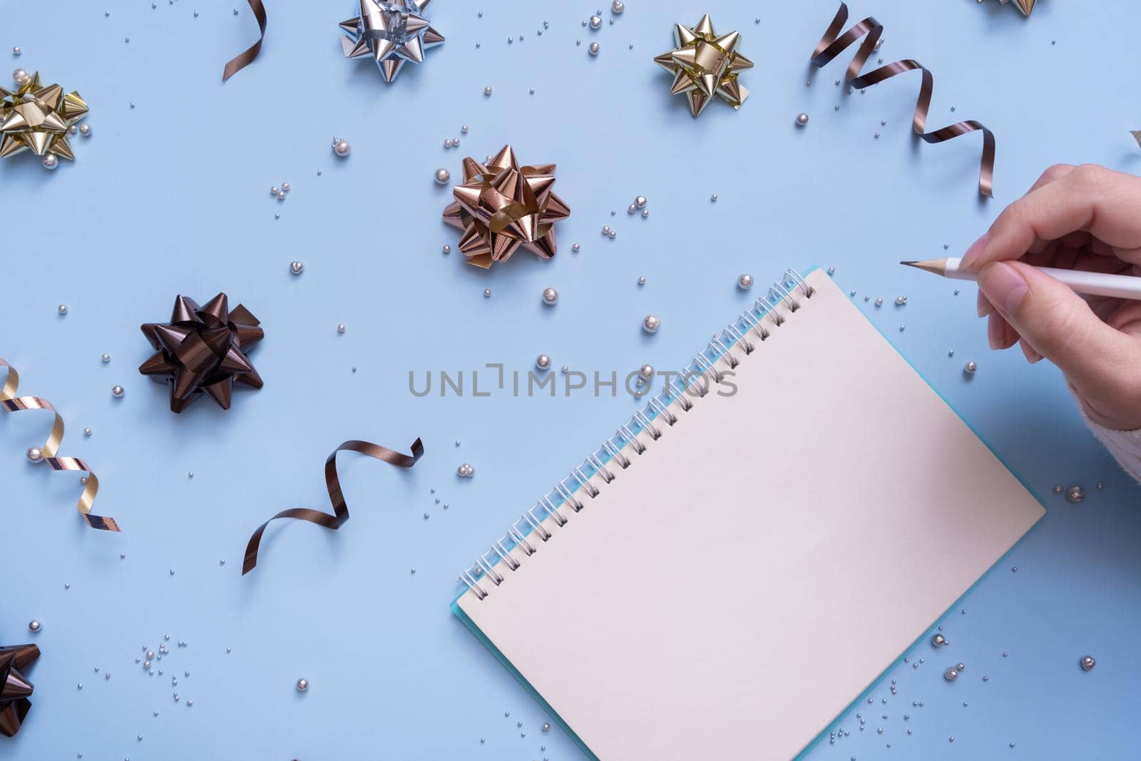 Tablet blank and pencil in female hand on bright festive background with bows and beads top view by ssvimaliss