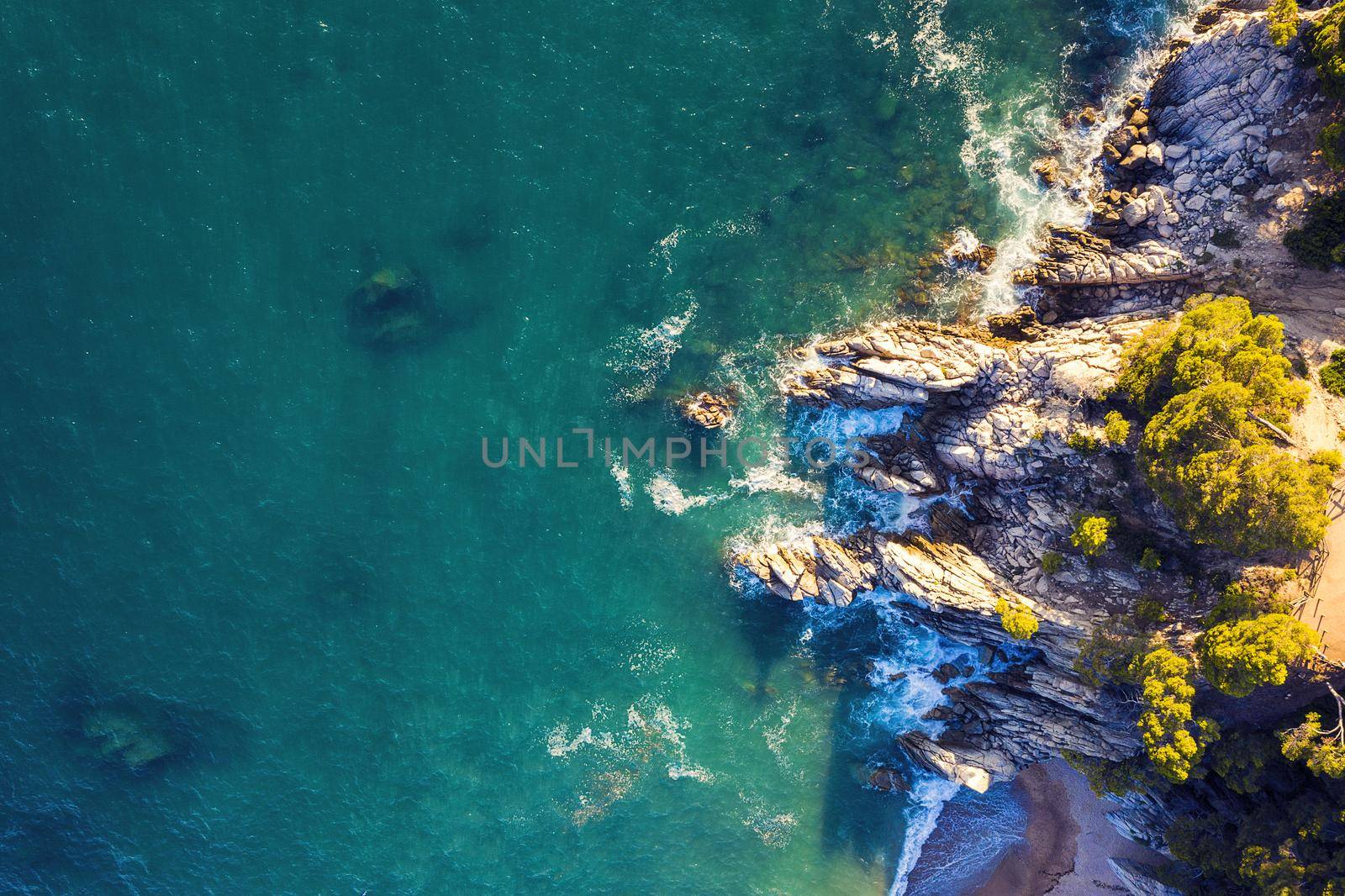 aerial top view of turquoise ocean with sea waves crashing on the rocky island coast with spray and foam, concept of adventure lifestyle and summer holidays in the wilderness