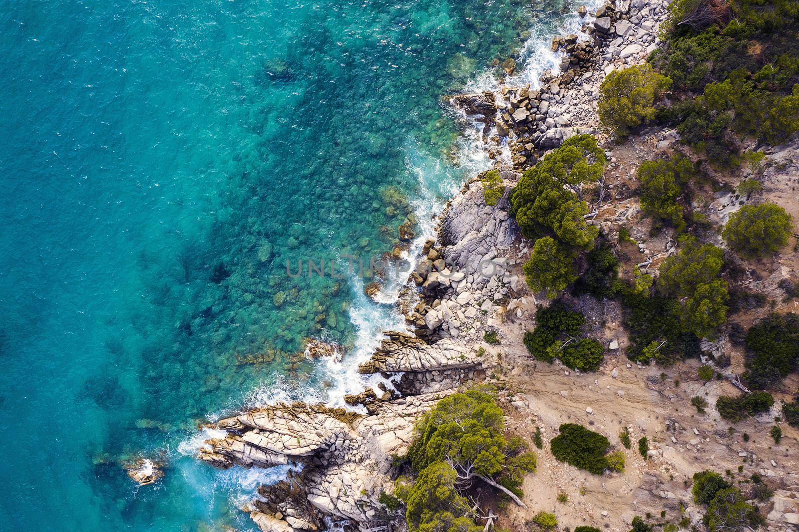 aerial top view of a clear ocean with beautiful sea waves crashing on the rocky island coast with spray and foam, concept of adventure lifestyle and summer holidays in the wilderness