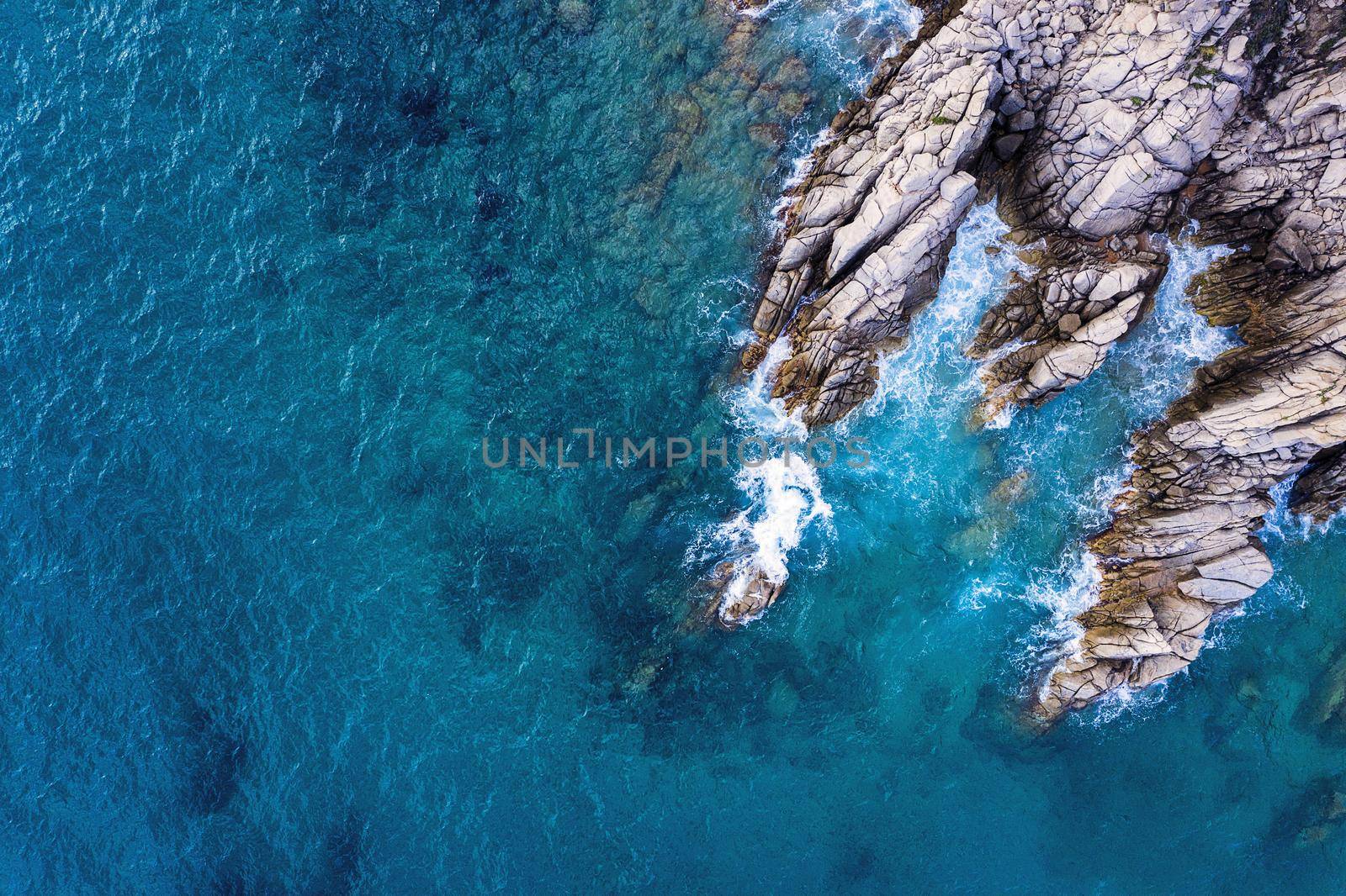 top view of clear turquoise ocean with sea waves hitting on the cliffs of the seashore of the rocky coast with spray and foam, power of the nature concept