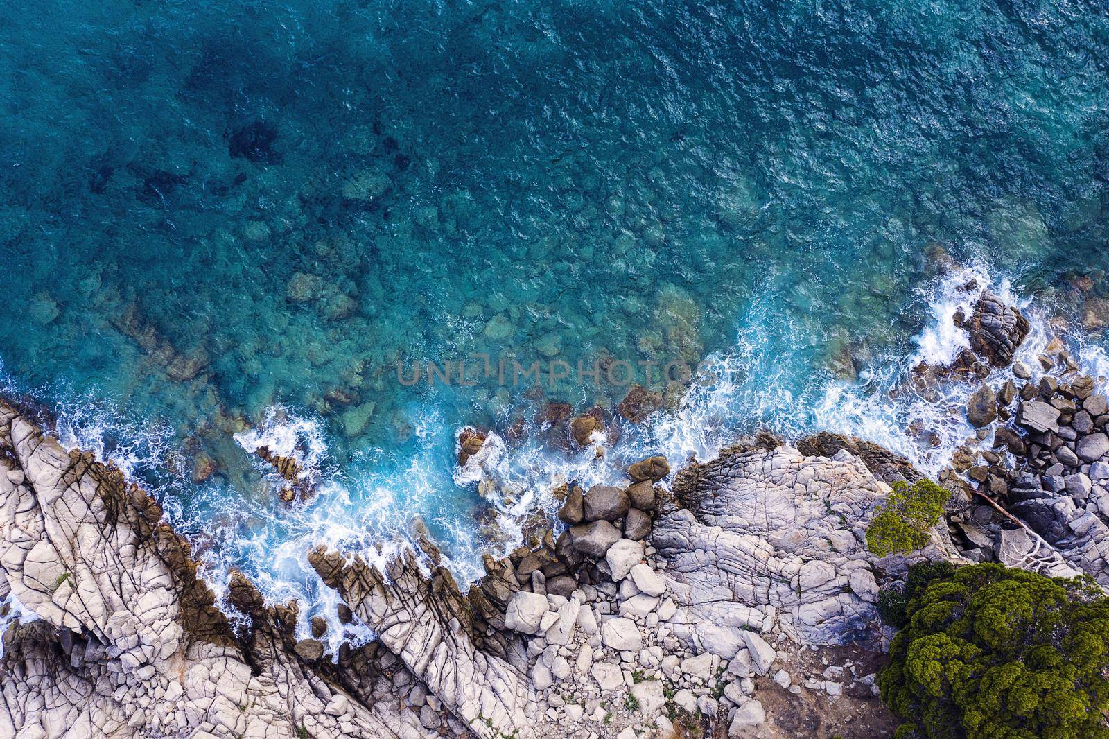 top view of clear blue ocean with sea waves hitting on the cliffs of the seashore of the rocky coast with spray and foam, power of the nature concept