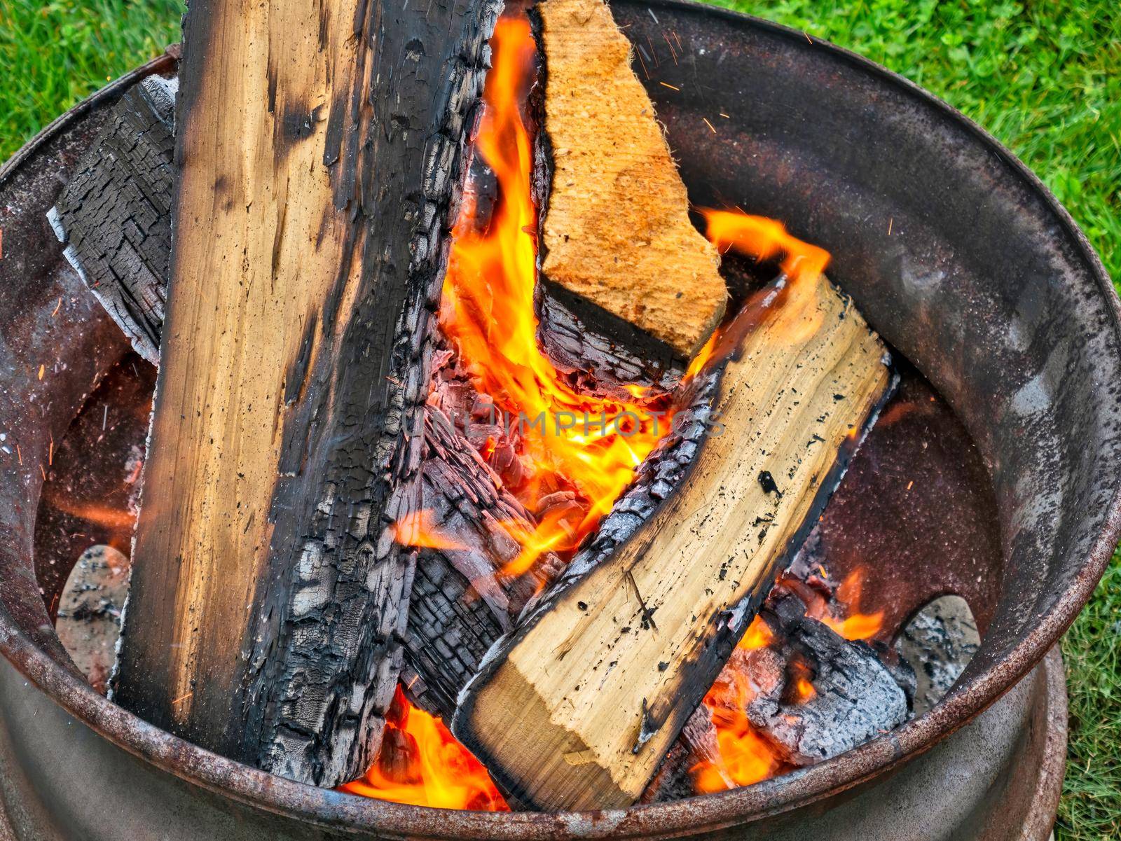 Campfire in a steel wheel on the concrete base and green lawn.