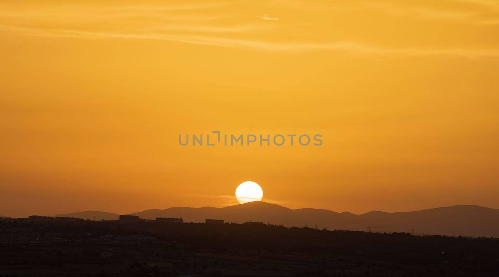 Big sun on sunset hiding behind mountains. Golden coloured sky. Copy space by papatonic