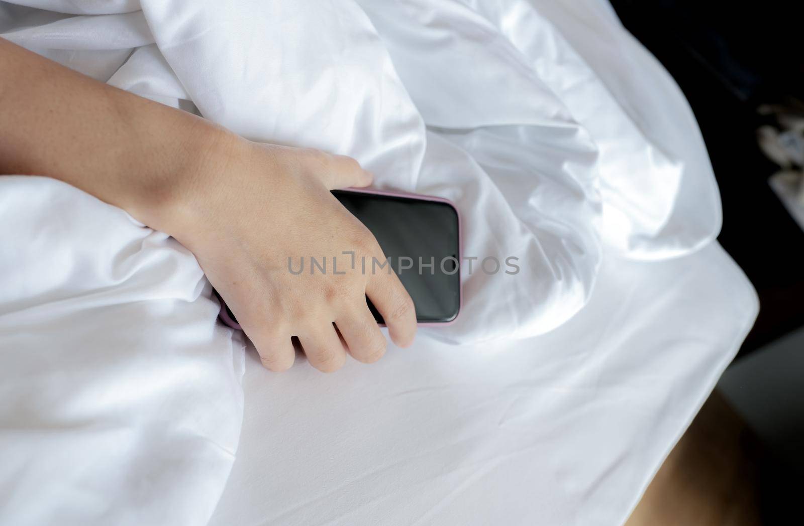 Woman sleeping in bed and hand holding mobile phone. Woman using smartphone in bedroom. Woman addicted using smartphone. Texting on cellphone with tired until falling asleep. Asleep with smartphone. by Fahroni