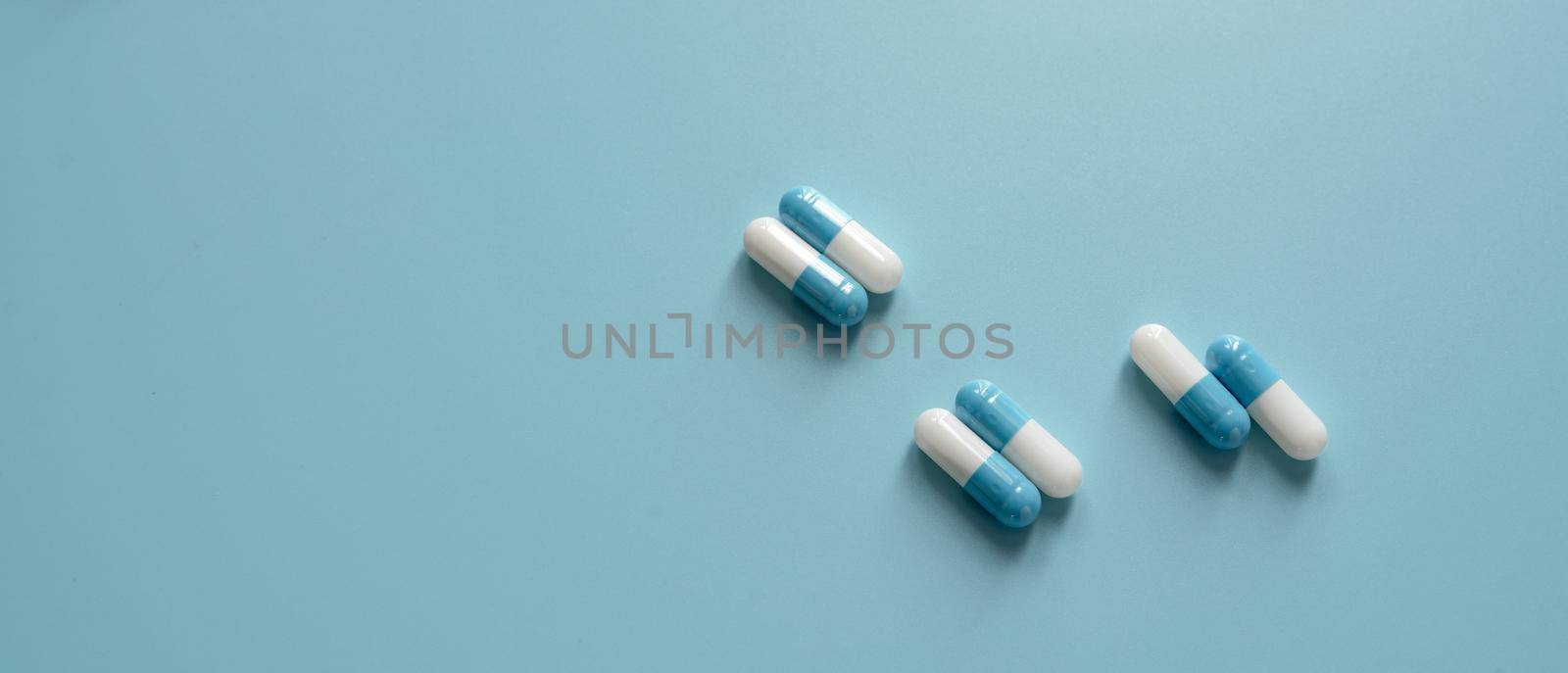 Blue and white capsule pills on blue background. Prescription drugs. Pharmaceutics background. Pharmaceutical industry. Dose of medicine for treating illness. Healthcare and medicine. Medical care.