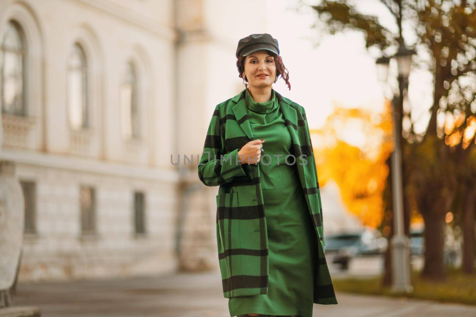 Outdoor fashion portrait of an elegant fashionable brunette woman, model in a stylish cap, green dress, posing at sunset in a European city in autumn. by Matiunina