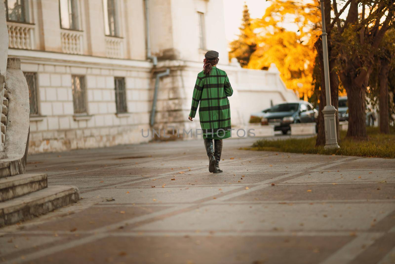 Outdoor fashion portrait of an elegant fashionable brunette woman, model in a stylish cap, green dress, posing at sunset in a European city in autumn