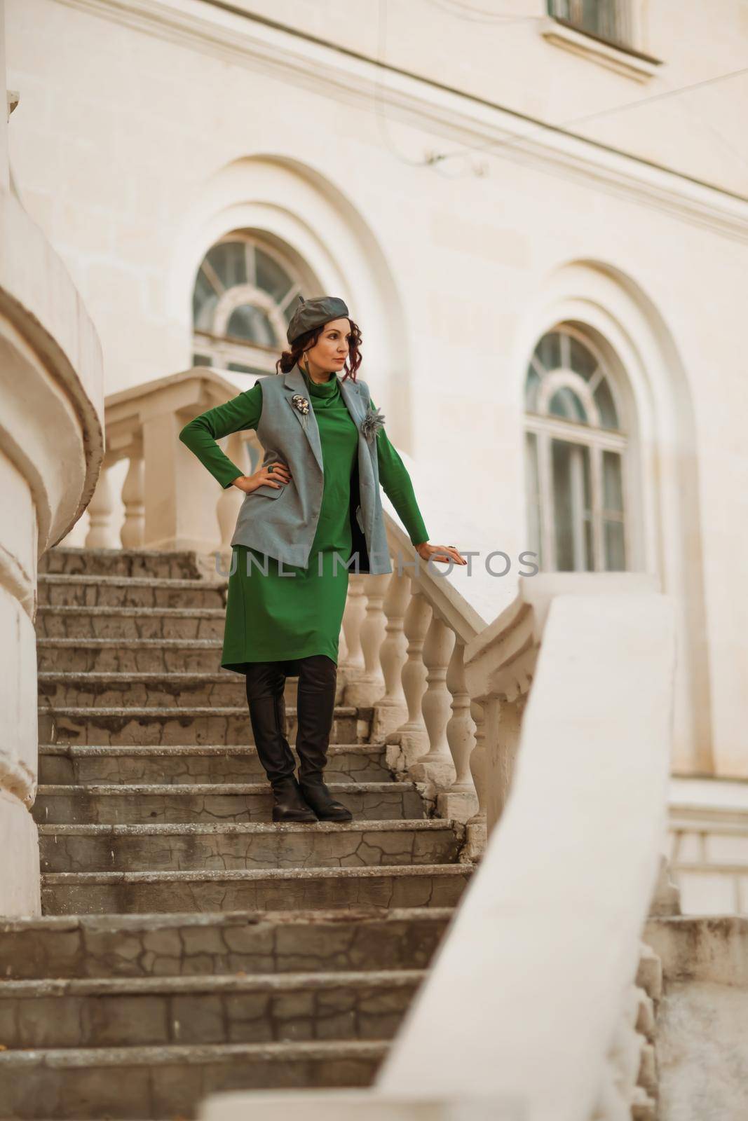 Outdoor fashion portrait of an elegant fashionable brunette woman, model in a stylish cap, green dress, posing at sunset in a European city in autumn