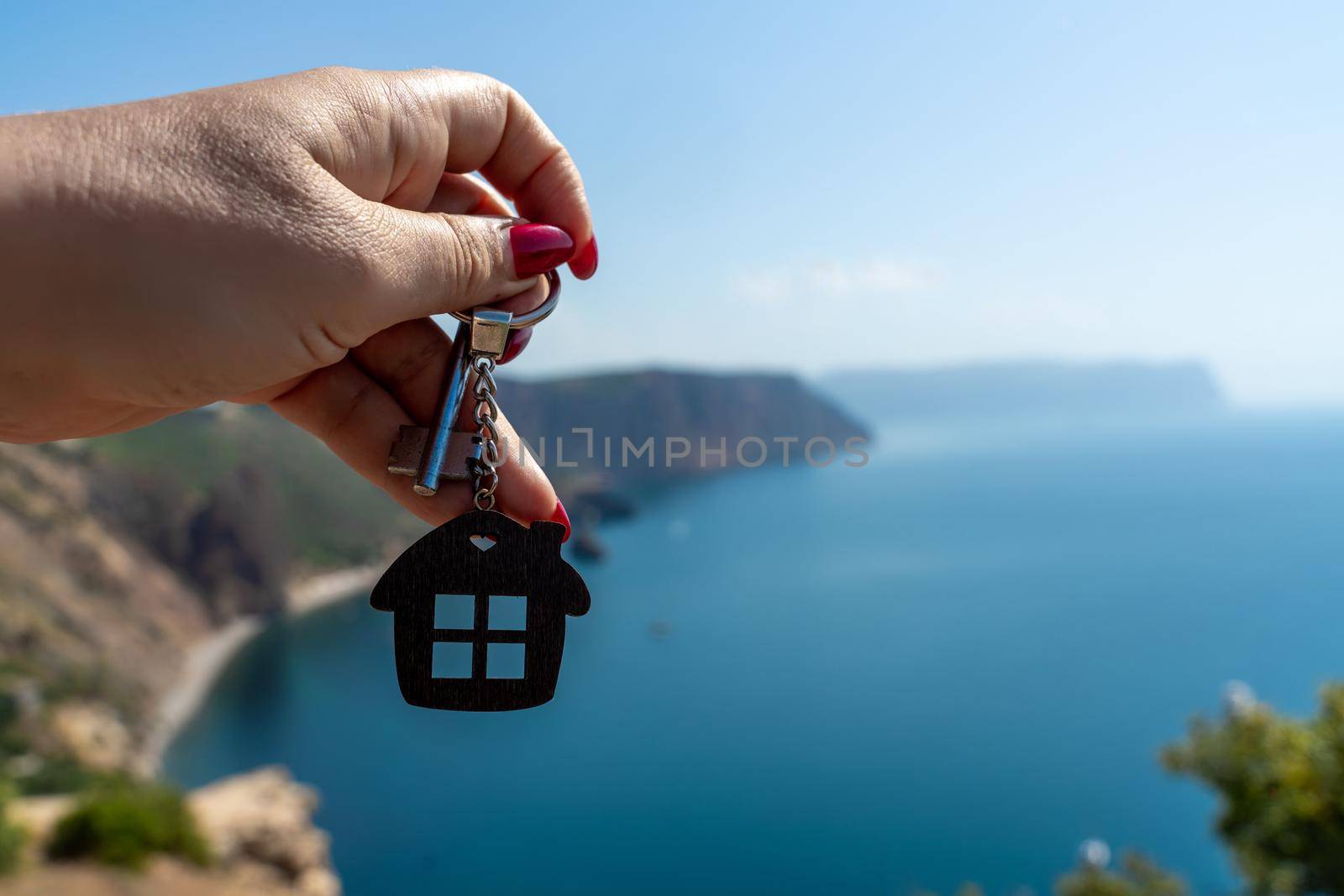 Keys with a keychain in the shape of a house in a female hand against the backdrop of the sea. The concept of buying a house, apartment, real estate, young family, mortgage loan, rental housing