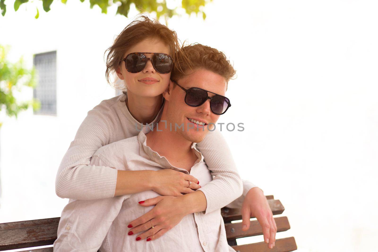Smiling beautiful woman and her handsome boyfriend. Woman embrace summer day. Happy cheerful couple in sunglasses walking old city park. Couple posing on the street near green tree