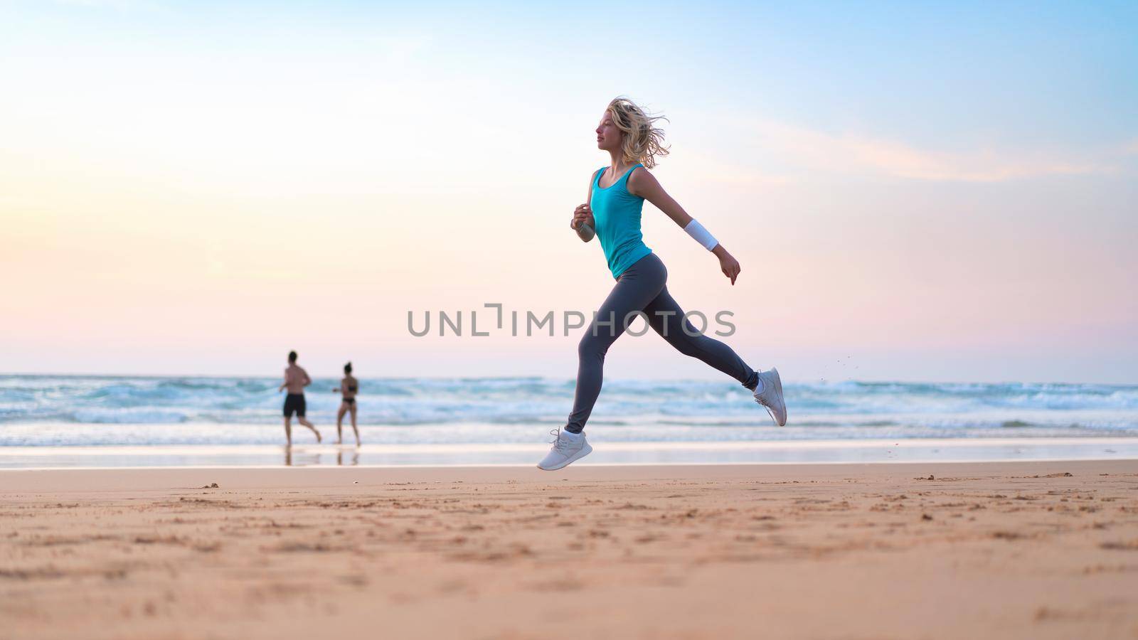 Active sporty woman run along ocean surf by water pool to keep fit and health. Sunset sand beach background with sun. Woman fitness, jogging workout and sport activity on summer family holiday.