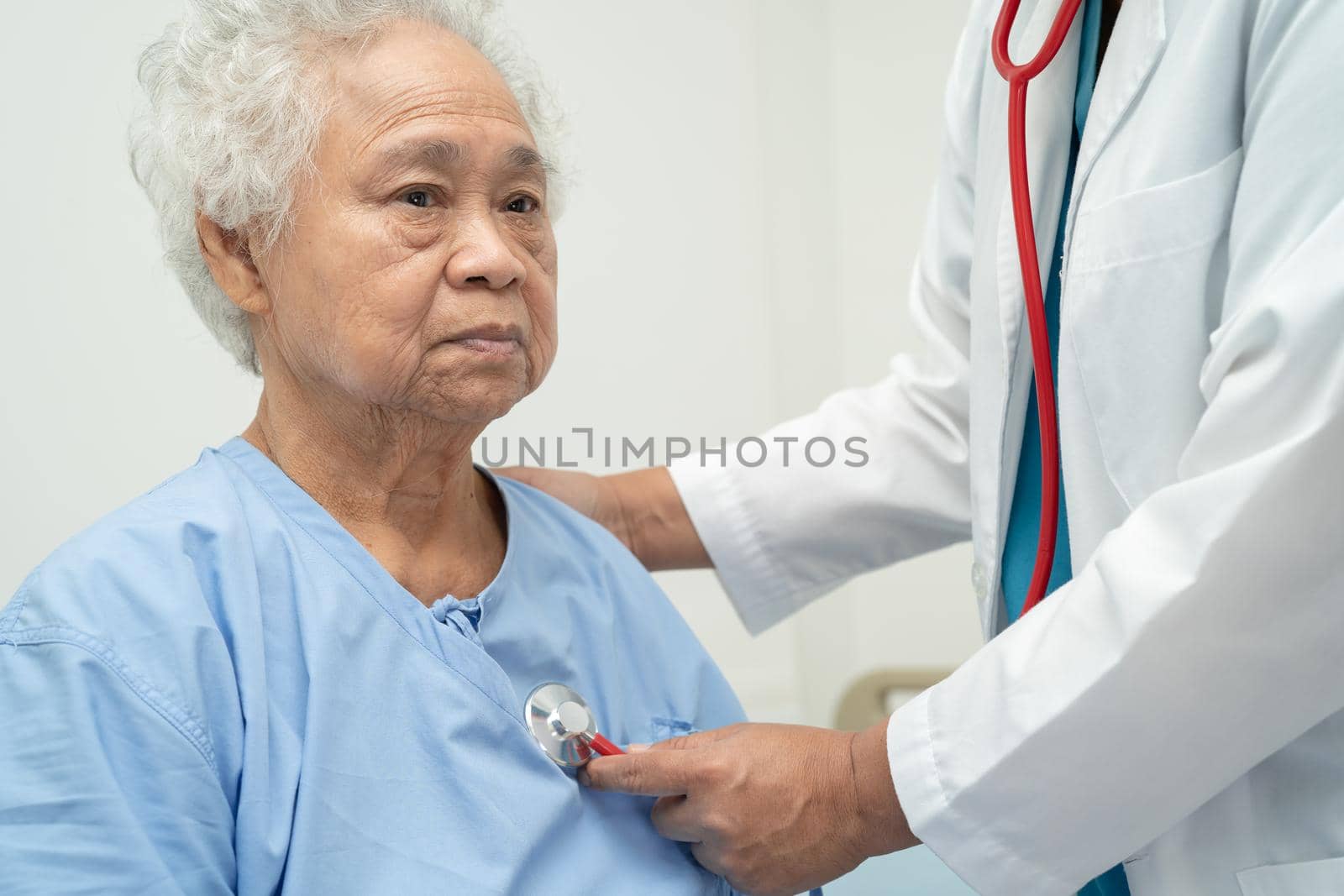 Doctor with stethoscope checking senior or elderly old lady woman patient while sitting on a bed in the nursing hospital ward, healthy strong medical concept.