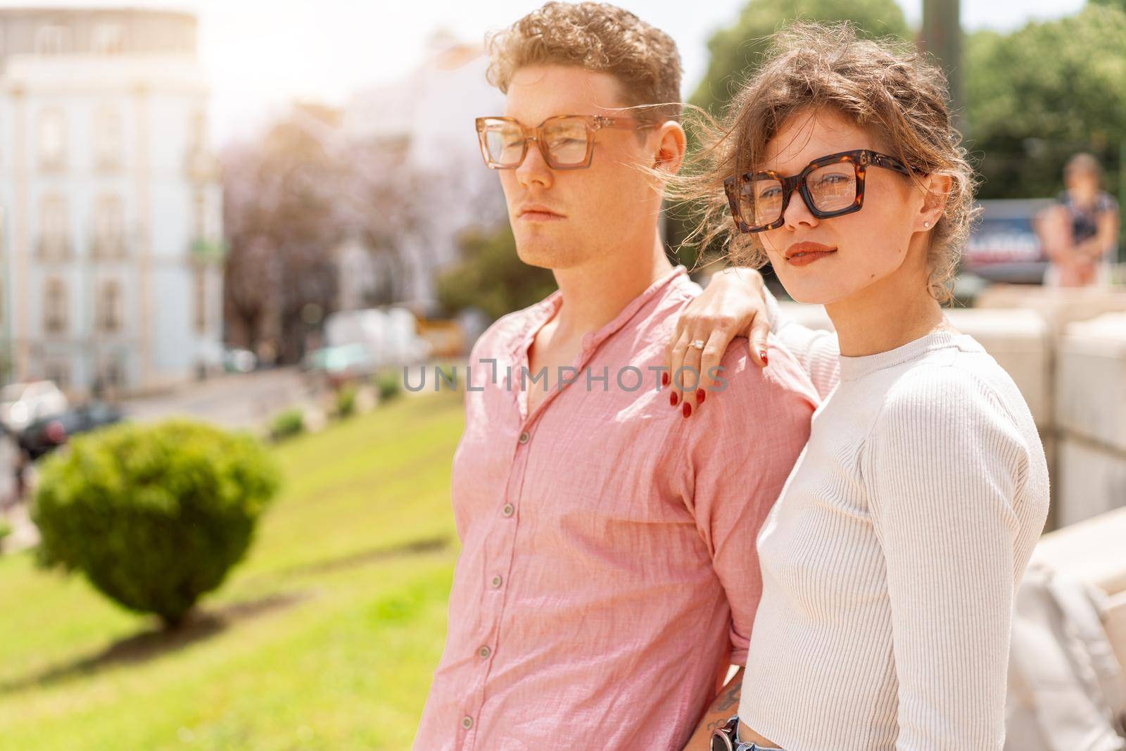 Young beautiful hipster couple in sunglasses in love walking on old city street by andreonegin