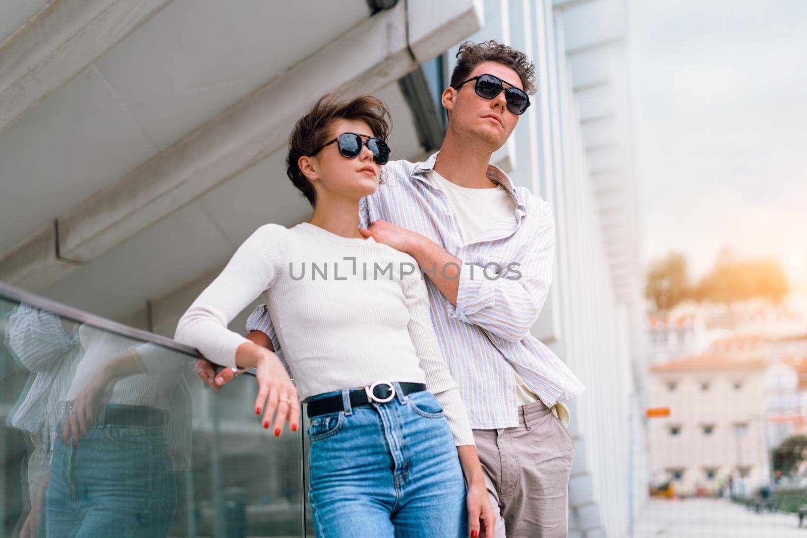 Smiling beautiful woman and her handsome boyfriend. Woman in casual summer jeans. Happy cheerful couple in sunglasses walking business district. Couple posing on the street modern building background