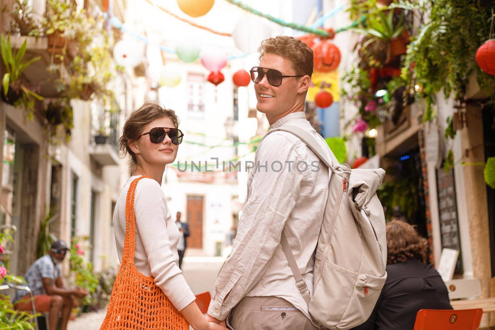 Young beautiful hipster couple in love walking on old city street with shopper and backpack, summer Europe vacation, travel, fun, happy, smiling, sunglasses, trendy outfit, romance, date, embracing