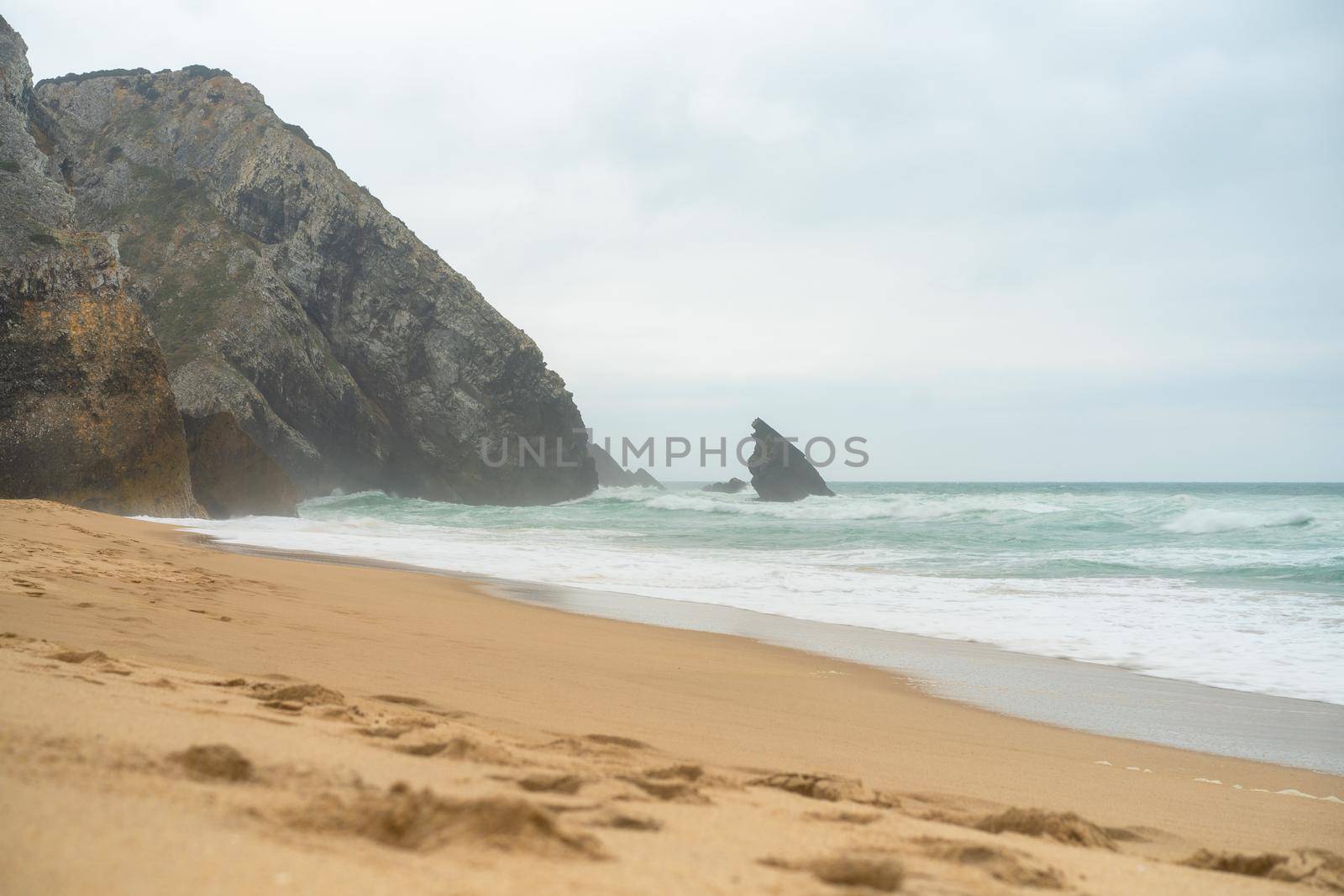 Ocean wild beach stormy weather. Praia da Adraga sandy beach with picturesque landscape background, Sintra Cascais, Portugal Handheld effect. Vitality of blue energy and clear ocean water