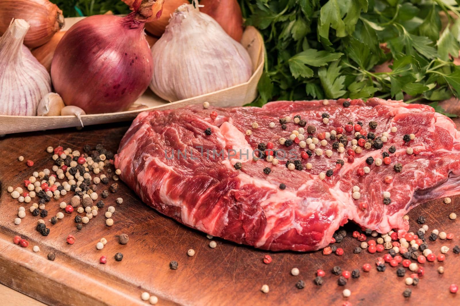 steak of beef on a wooden board with spices pepper parsley salt onions shallots garlic