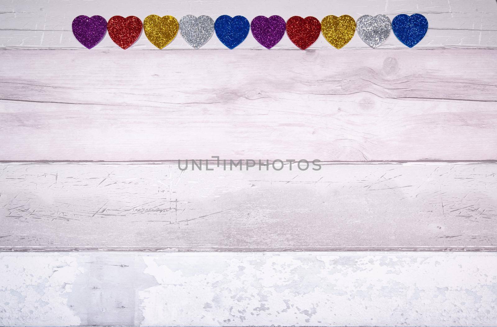 Hearts with glitter of all colors on a background of old wooden planks resembling an old parquet floor. Concept of valentines day and love in general.