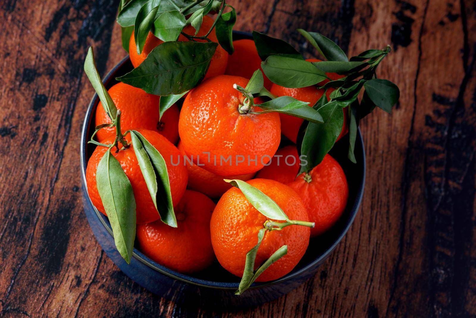 Clementines with leaves in a blue ceramic dish on an old wooden table by jp_chretien