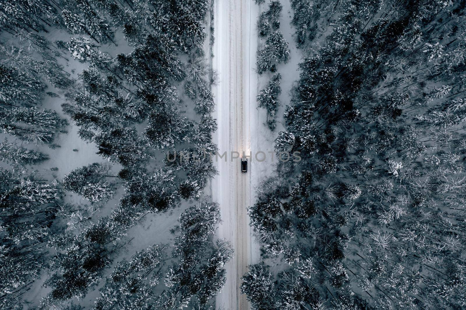 Night time aerial view of snowy road in pine tree forest in winter season. Drone top down view of snowy winter road surrounded pine and fir forest and two cars with light