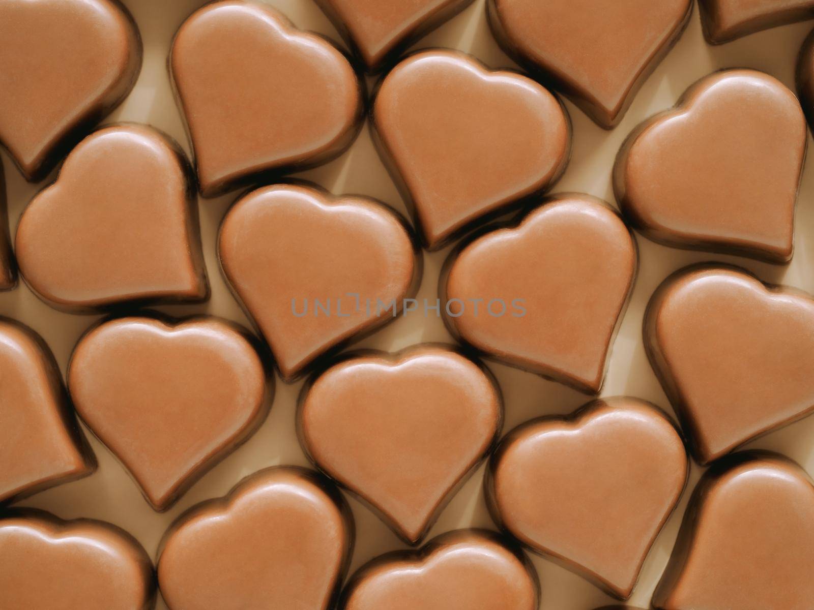 Pattern of romantic chocolate confections in heart shapes on pastel yellow background. Pattern of heart milk chocolate praline sweets on champagne beige background. Top view or flat lay