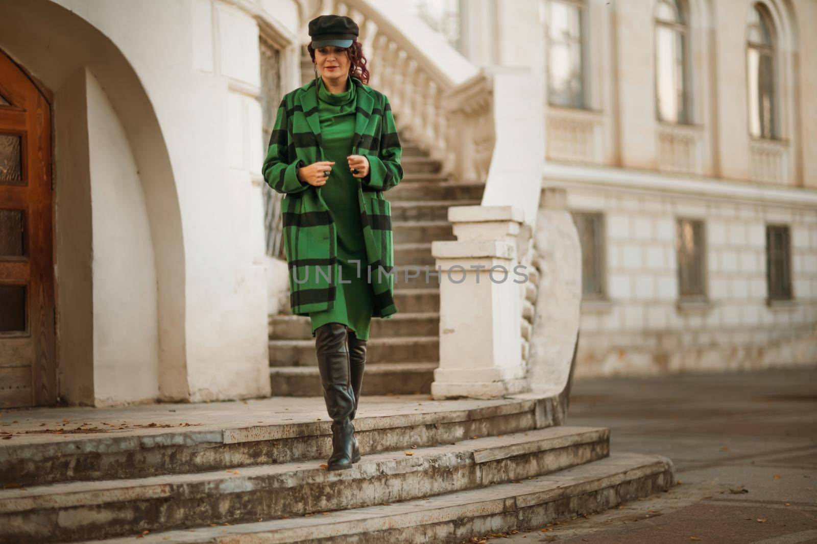 Outdoor fashion portrait of an elegant fashionable brunette woman, model in a stylish cap, green dress, posing at sunset in a European city in autumn. by Matiunina