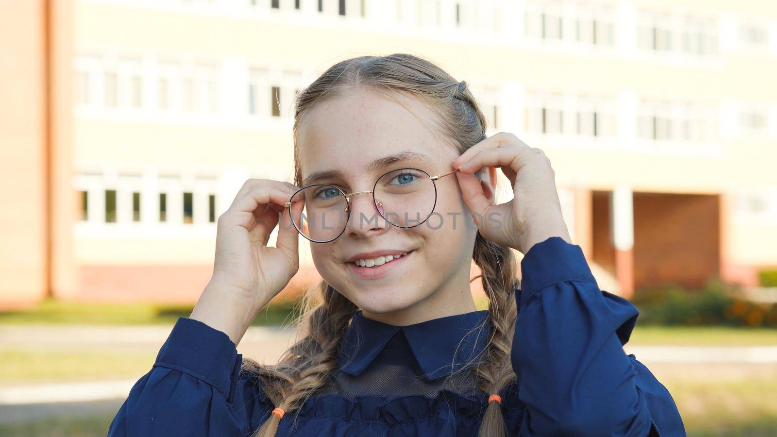 A teenage girl wearing glasses in front of a school