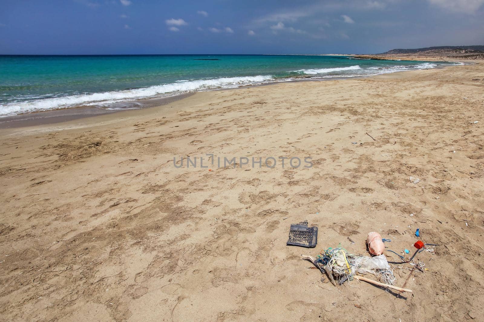 Beautiful wild natural beach, no people, calm azure sea in background, pile of garbage in foreground. Marine pollution concept.