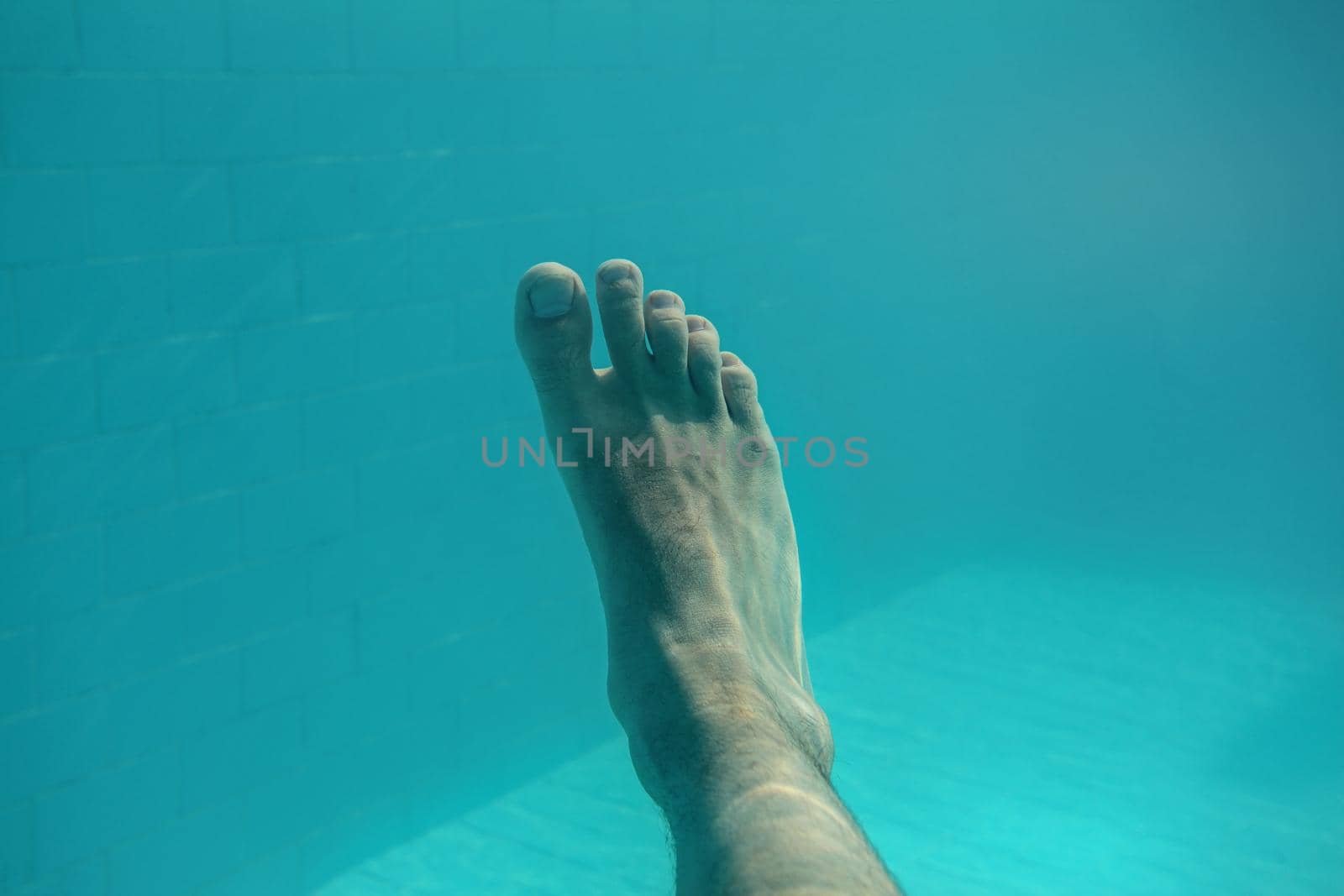 Underwater photo - man's single foot with light blue swimming pool tiles in background.