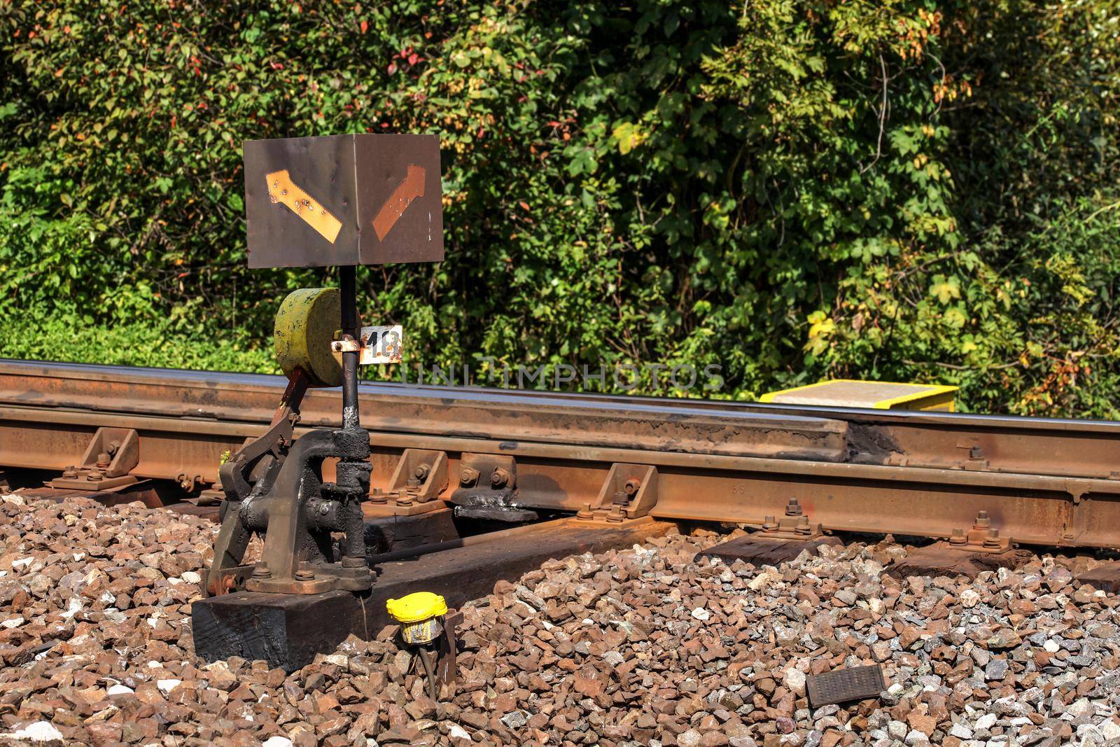 Old railway cross switch covered with black oil and dirt. Rail tracks and green bushes in background.