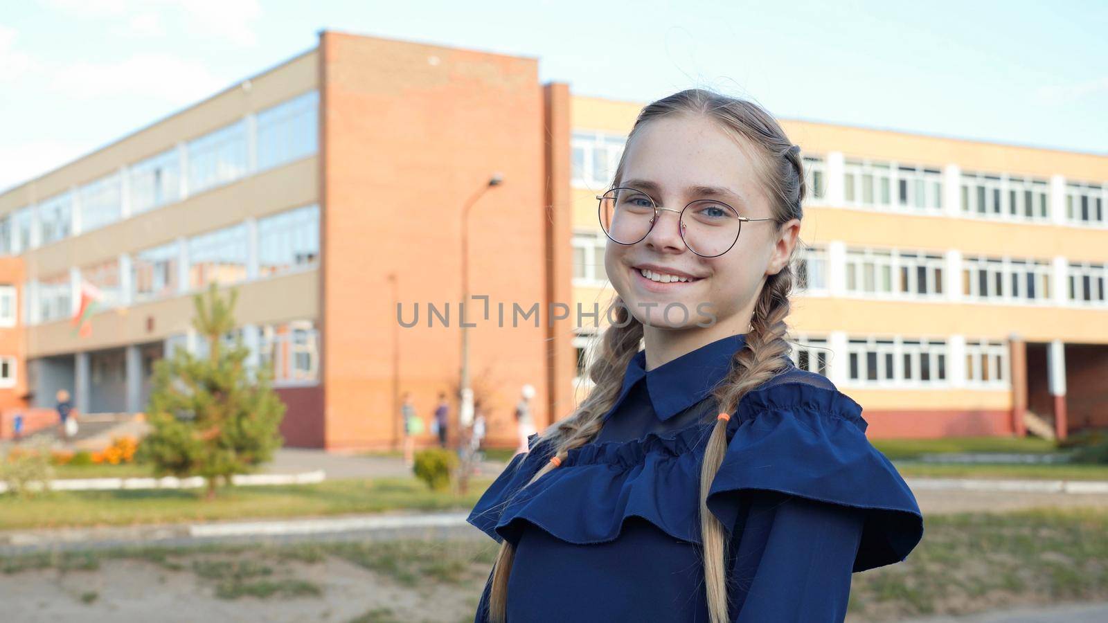 A teenage girl wearing glasses in front of a school