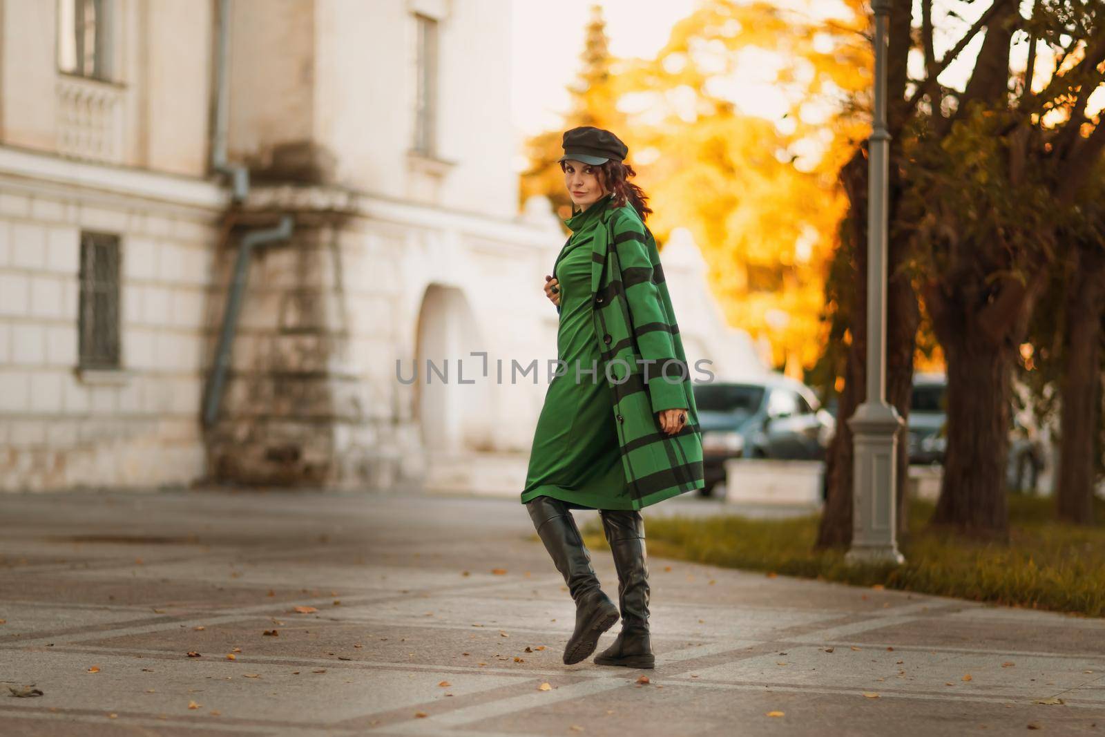 Outdoor fashion portrait of an elegant fashionable brunette woman, model in a stylish cap, green dress, posing at sunset in a European city in autumn. by Matiunina