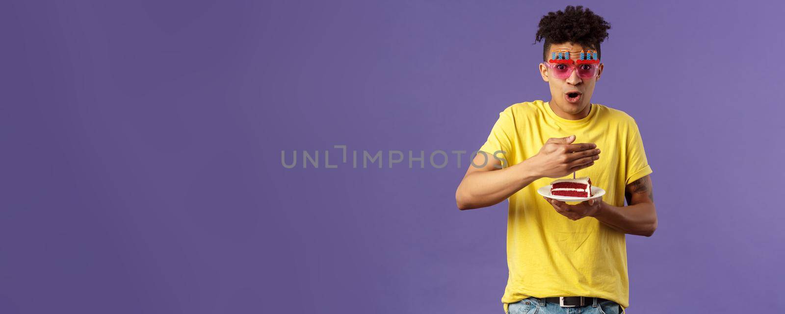 Celebration, party and holidays concept. Portrait of happy funny, enthusiastic young man celebrating birthday, protect lit candle on b-day cake from wind, making wish, smiling cheerful.