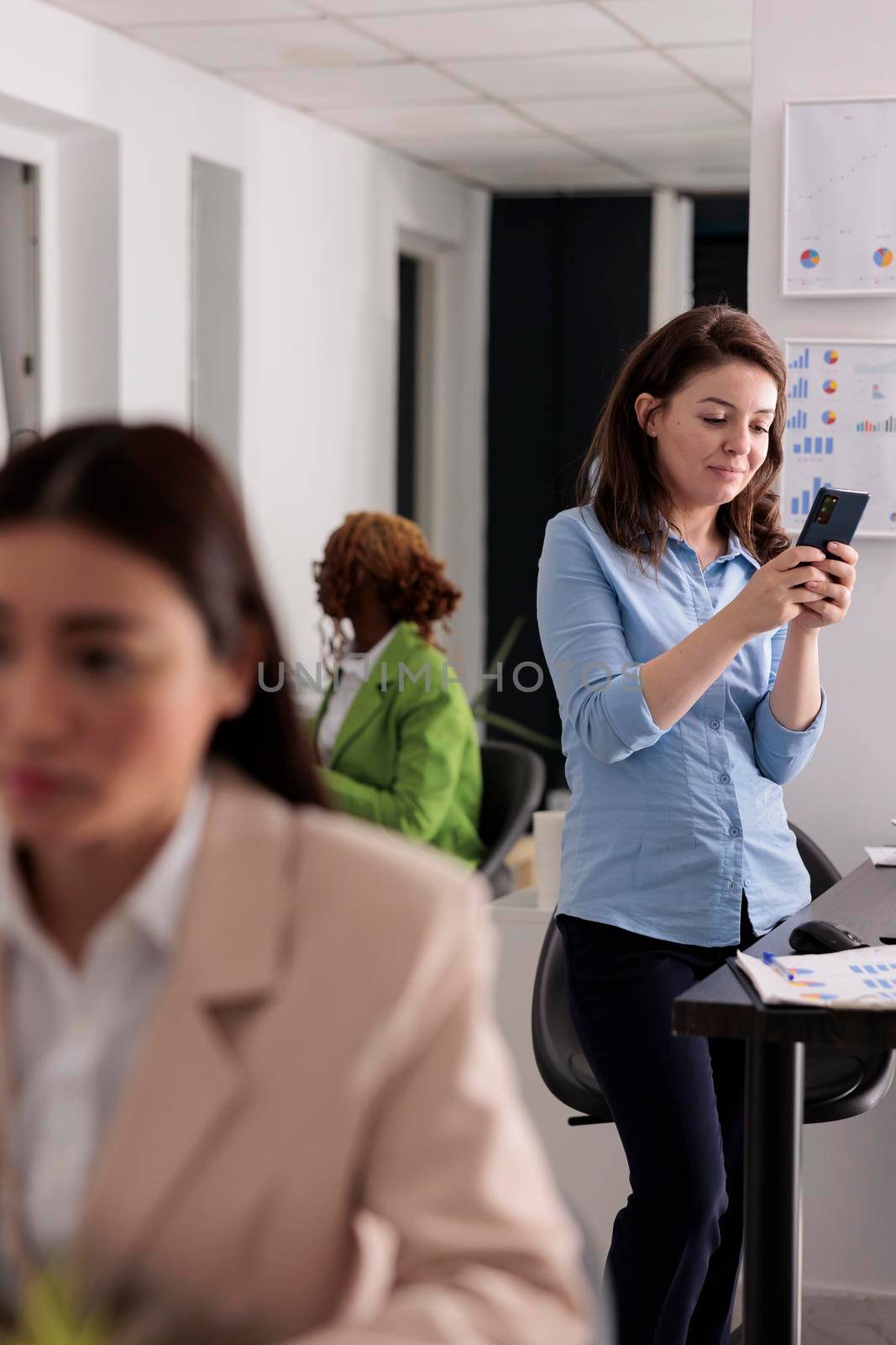 Smiling employee sending messages on smartphone, standing near workplace by DCStudio
