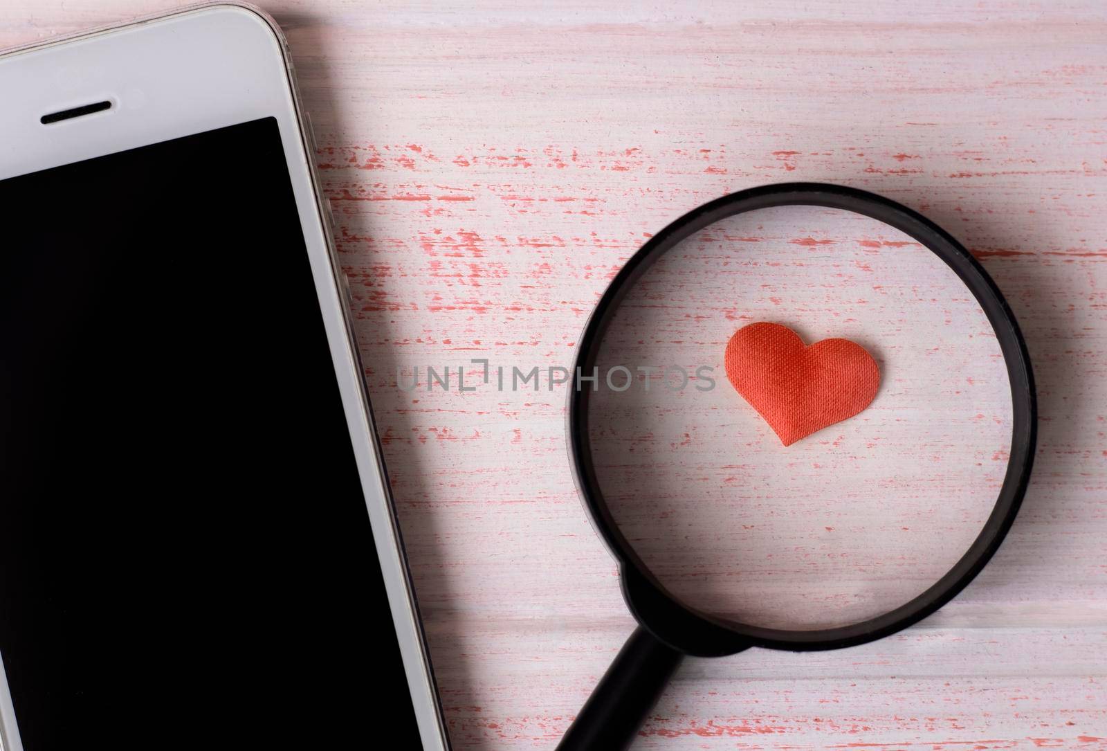 heart under a magnifying glass, lies near a white mobile phone. by Suietska