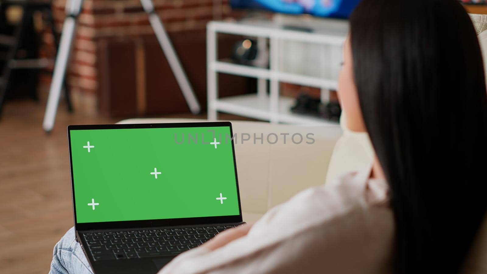 Woman having laptop with green screen chroma key template display while sitting on sofa at home. Person with computer having mockup isolated background while in apartment.