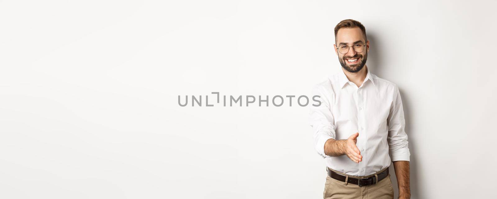 Confident businessman extending hand for handshake, greeting business partner and smiling, standing over white background.