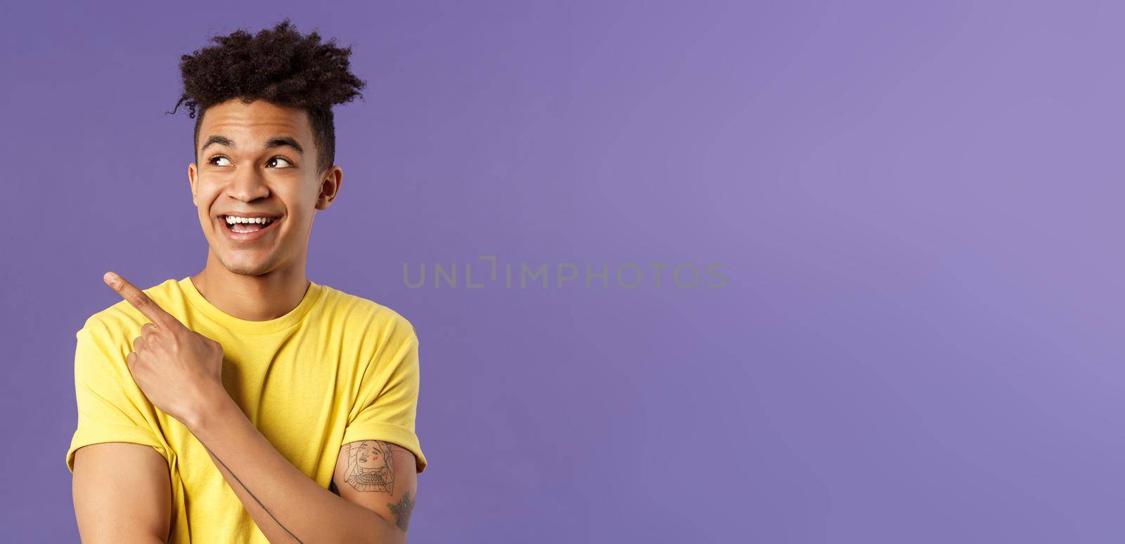 Close-up portrait of funny cute hispanic man with dreads, laughing and smiling at something, pointing looking upper left corner enthusiastic expression, purple background.