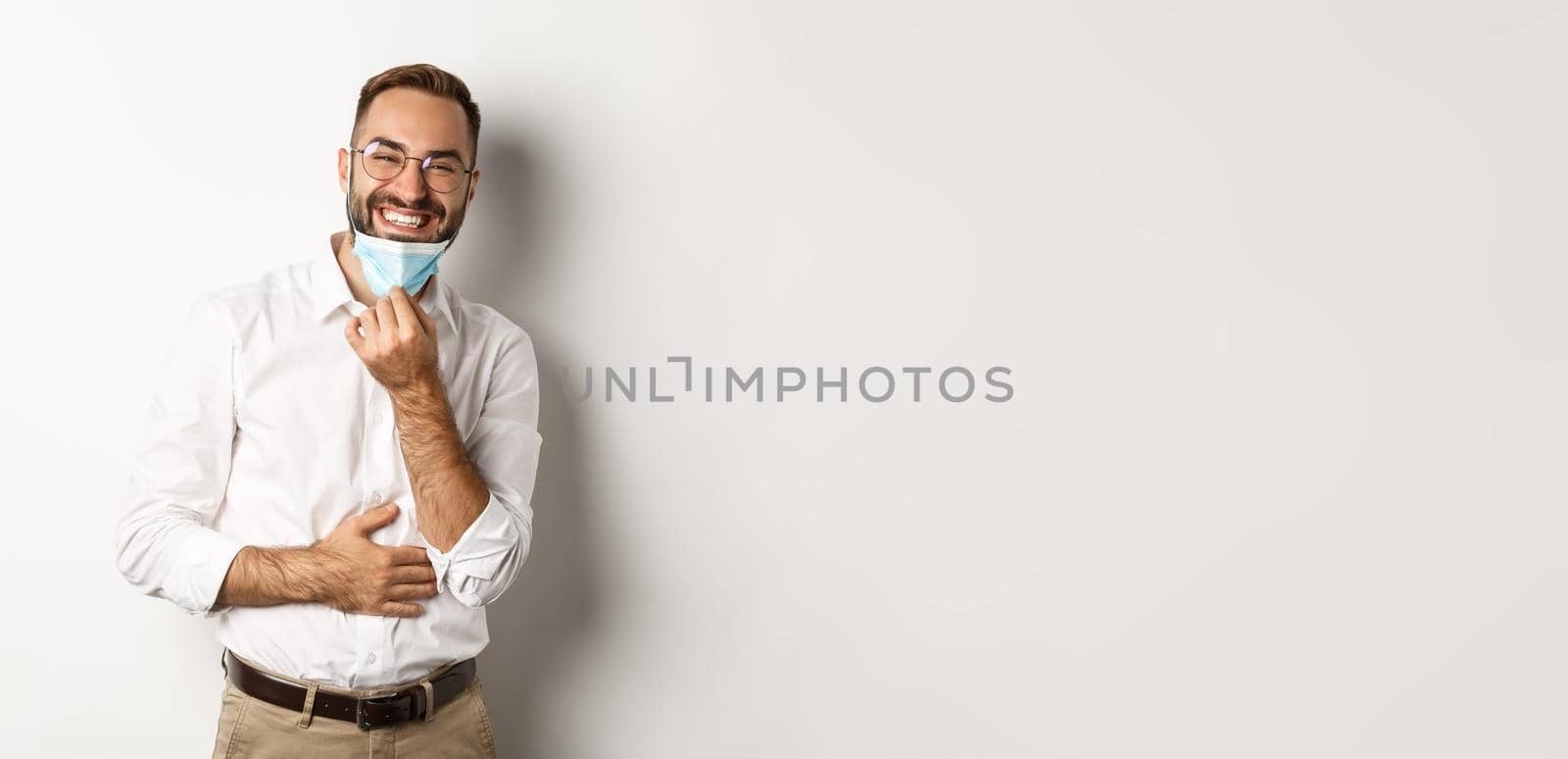 Covid-19, social distancing and quarantine concept. Happy businessman take off face mask and smiling, standing over white background by Benzoix