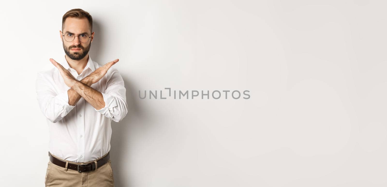 Angry businessman frowning and showing cross, stop you, telling no and prohibit something, standing over white background.