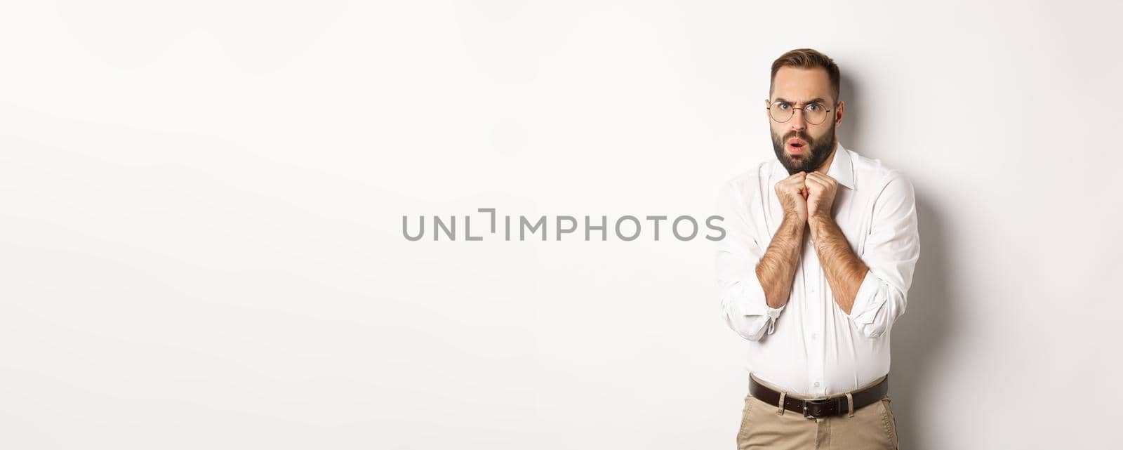 Scared and timid businessman looking anxious, trembling from fear, standing over white background.